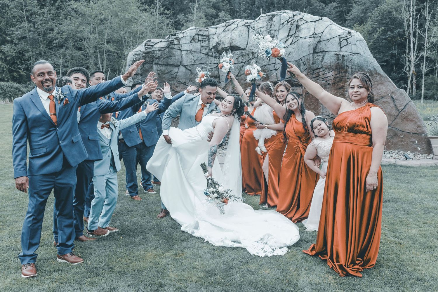 Wedding party members in orange dresses and navy suits perform playful dipping poses during outdoor photo session.