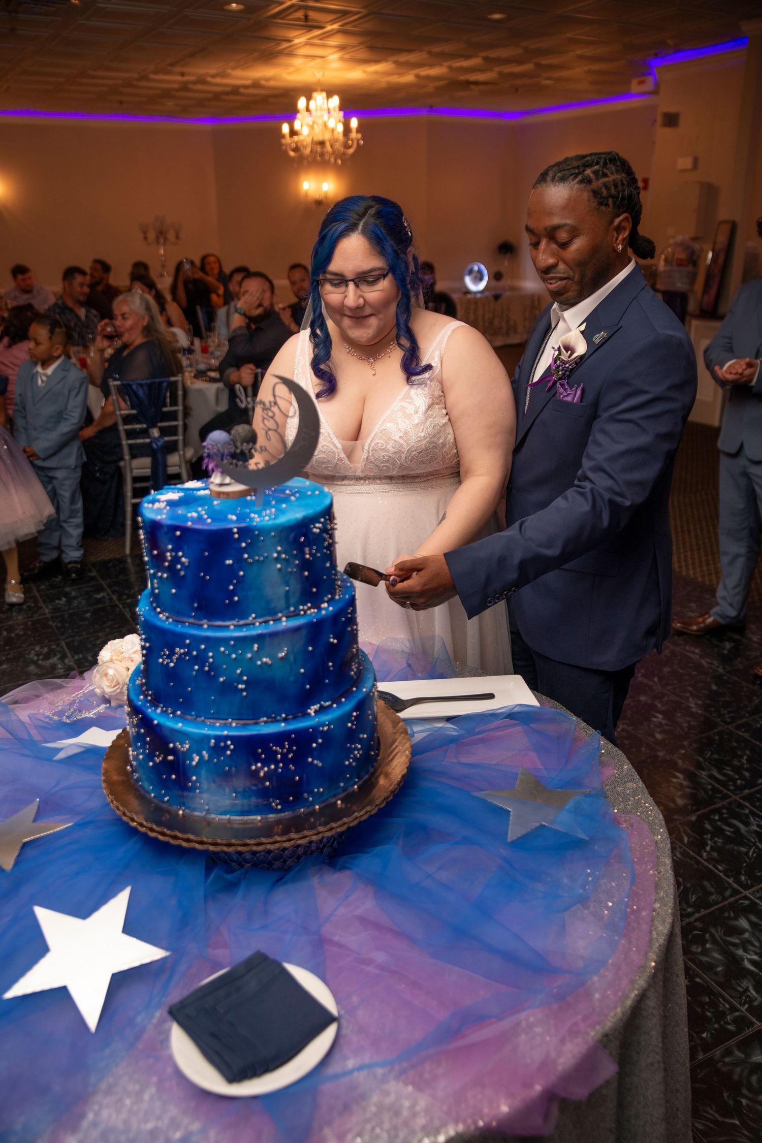 A wedding cake cutting sequence showing a blue starry-themed tiered cake with white stars on a purple-lit table.