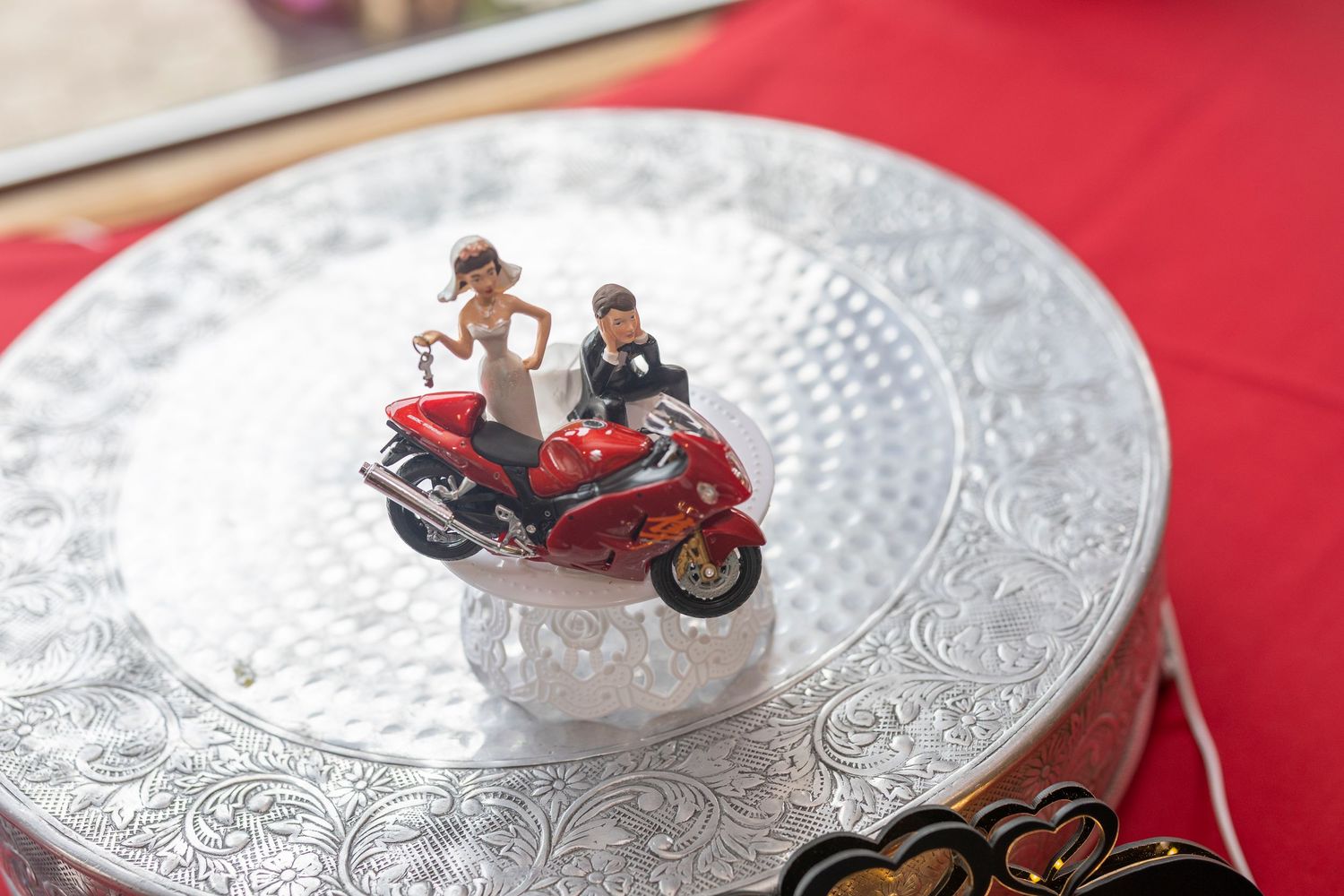 A miniature motorcycle figurine with two riders displayed on a decorative silver plate with intricate patterns.