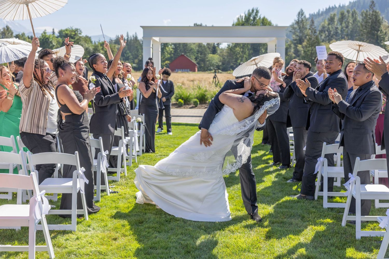 Joyful wedding ceremony outdoors with white parasols and guests celebrating on a sunny day by mountain scenery.
