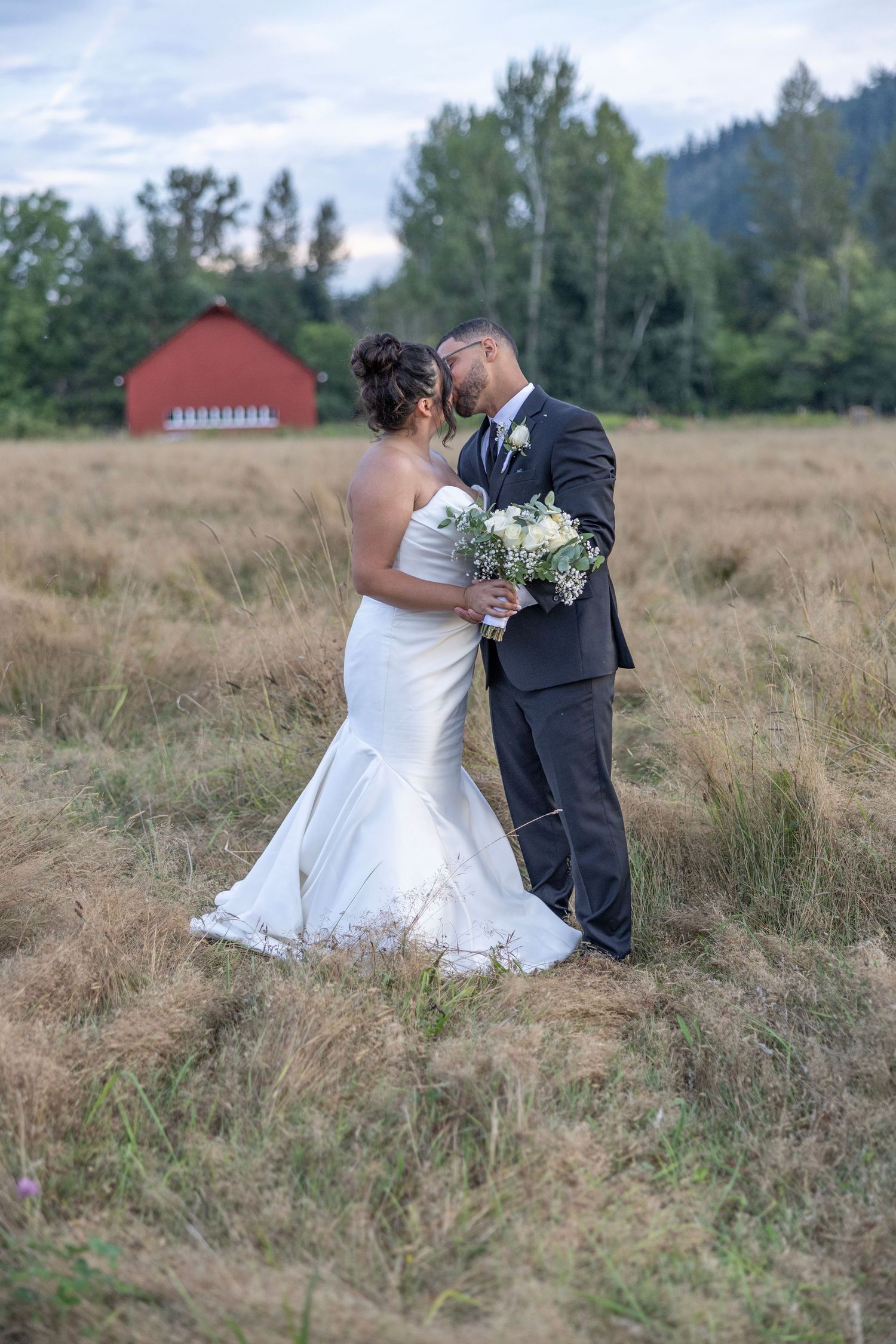 A couple in wedding attire shares an intimate moment in a rustic field of tall grass during their outdoor ceremony.