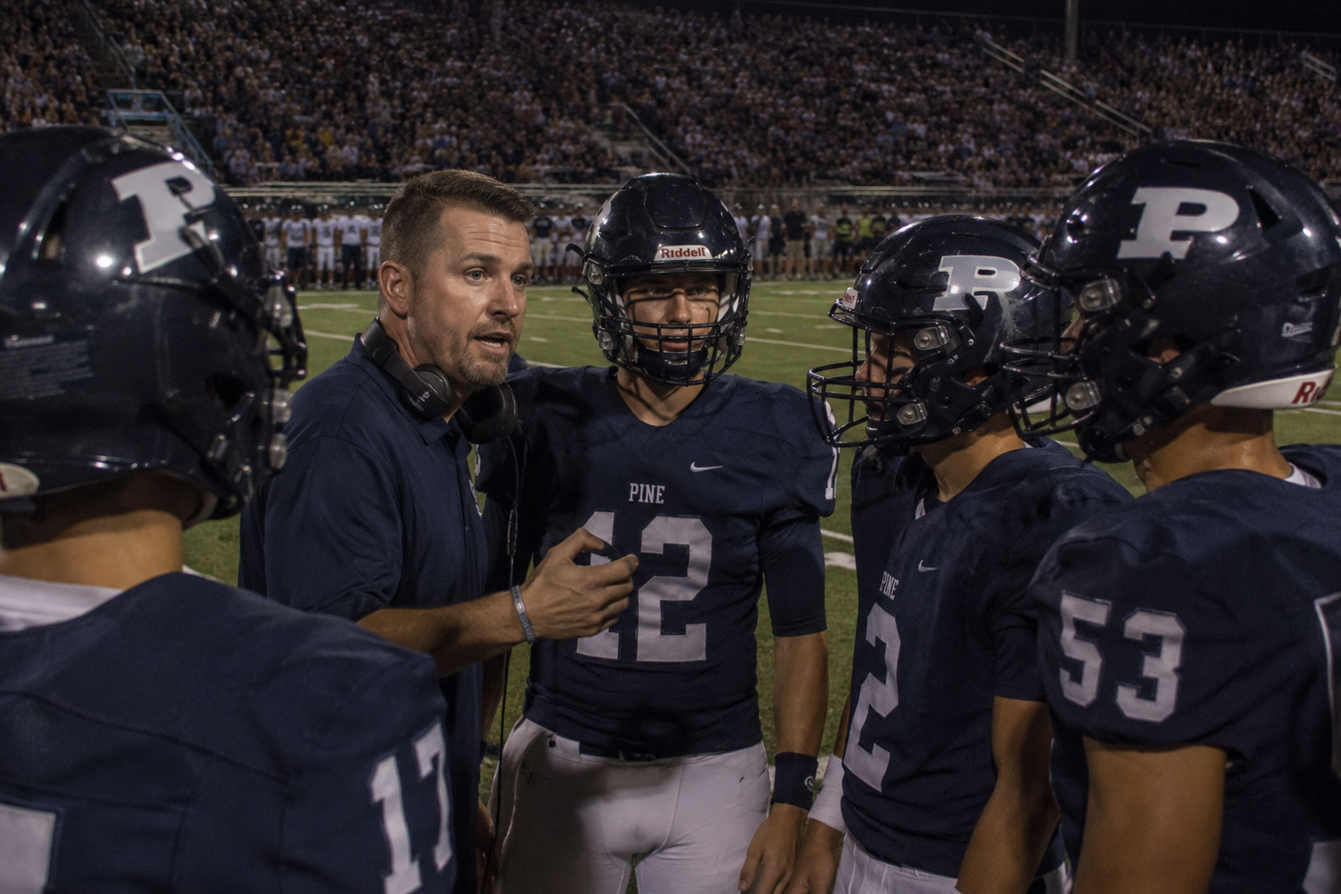 A football coach talks to player #42 on the sideline during a night game under bright stadium lights.