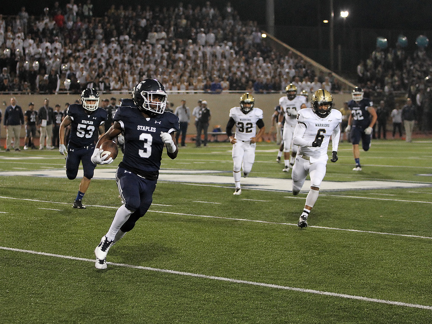Football player number 3 sprints down the sideline for a long run during a night game.