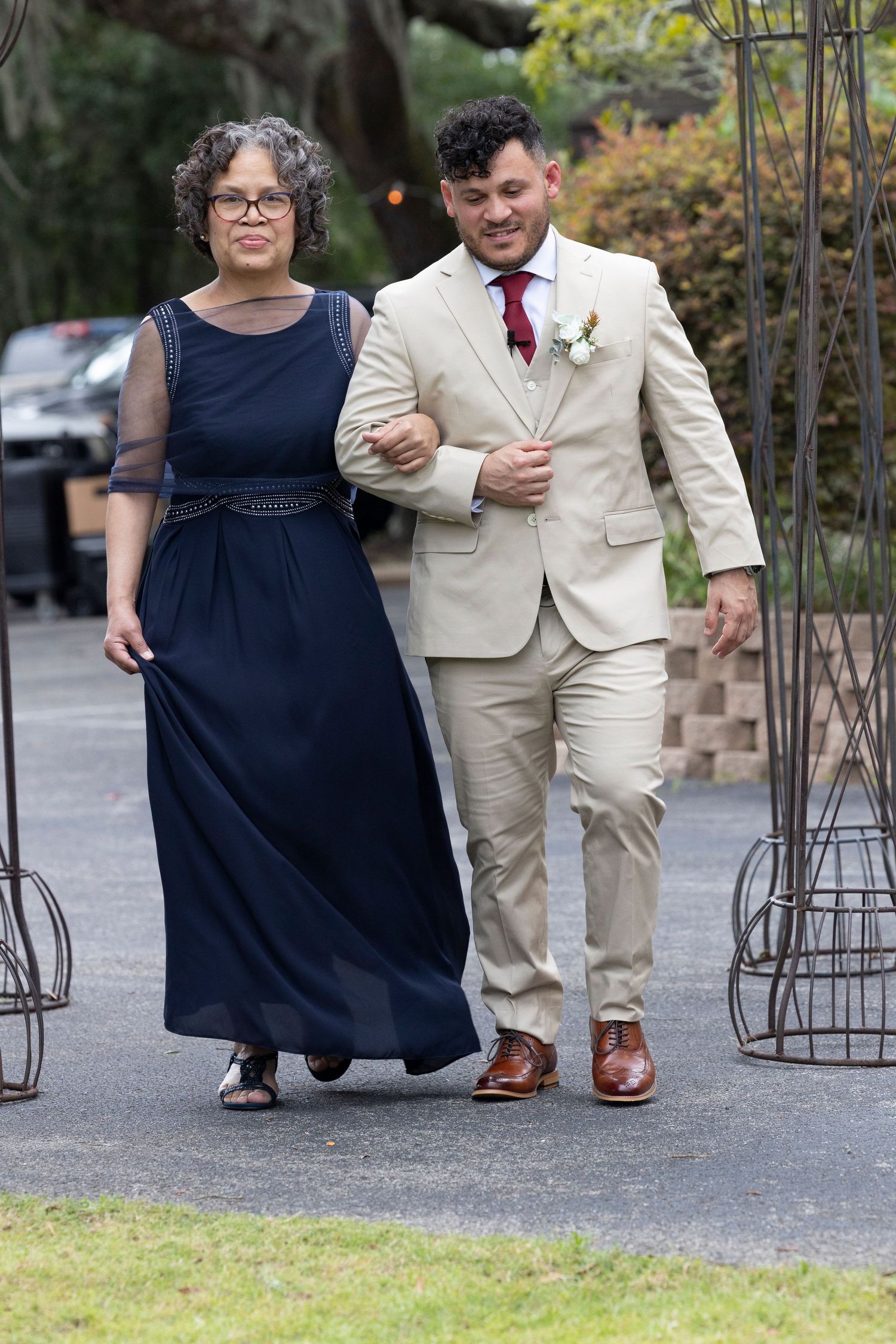 Two people walking arm in arm at a formal event, with one wearing a navy dress and another in a tan suit.