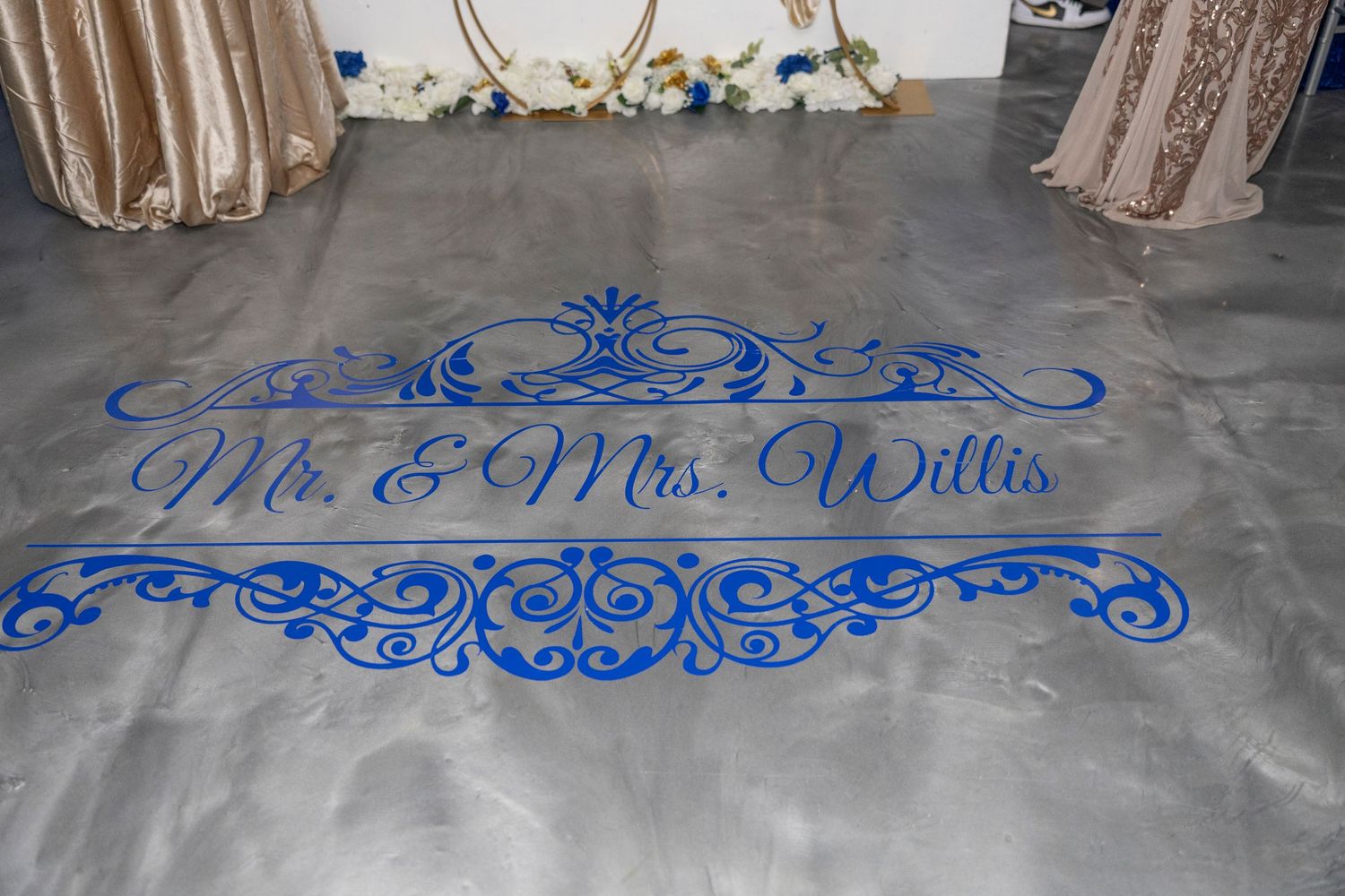 Elegant blue monogram dance floor decal reading Mr. & Mrs. Willis with ornate scrollwork design at a wedding reception.