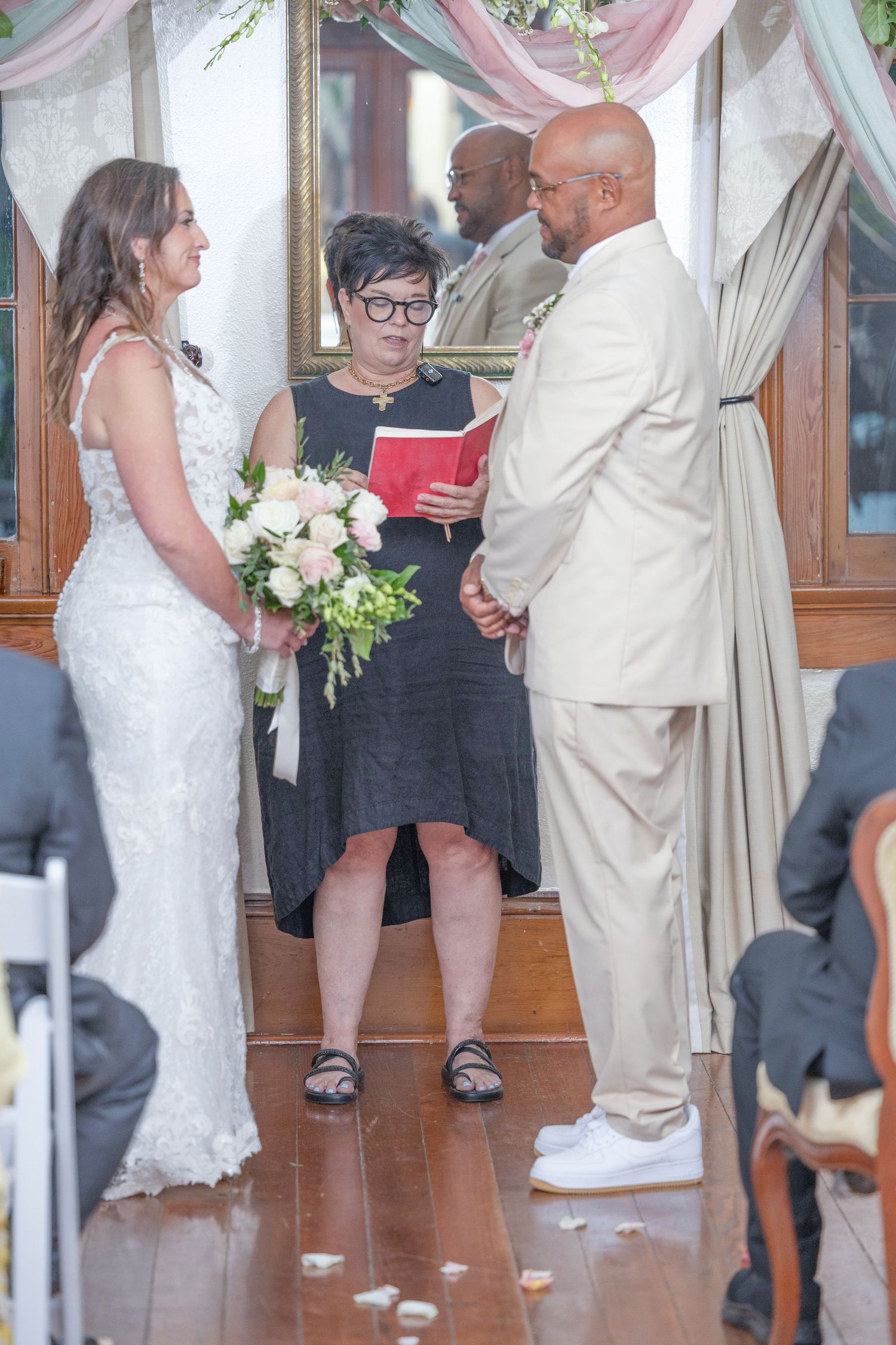 A wedding ceremony takes place indoors with the couple and guests gathered around in formal attire.