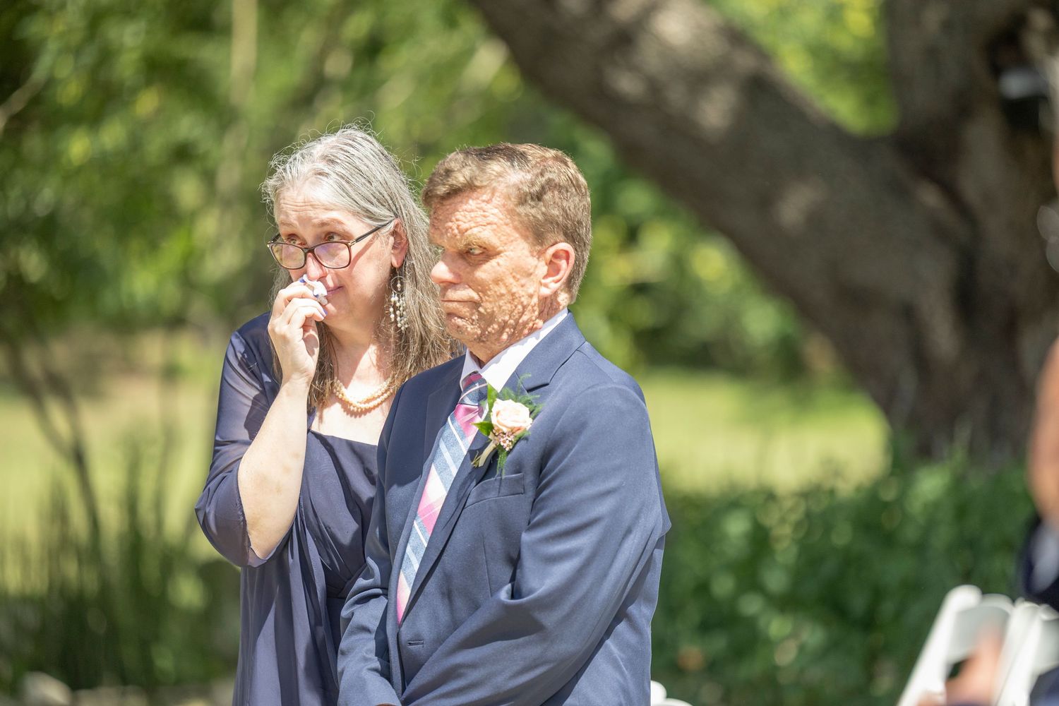 Two people share an intimate moment in a garden setting during a wedding ceremony.