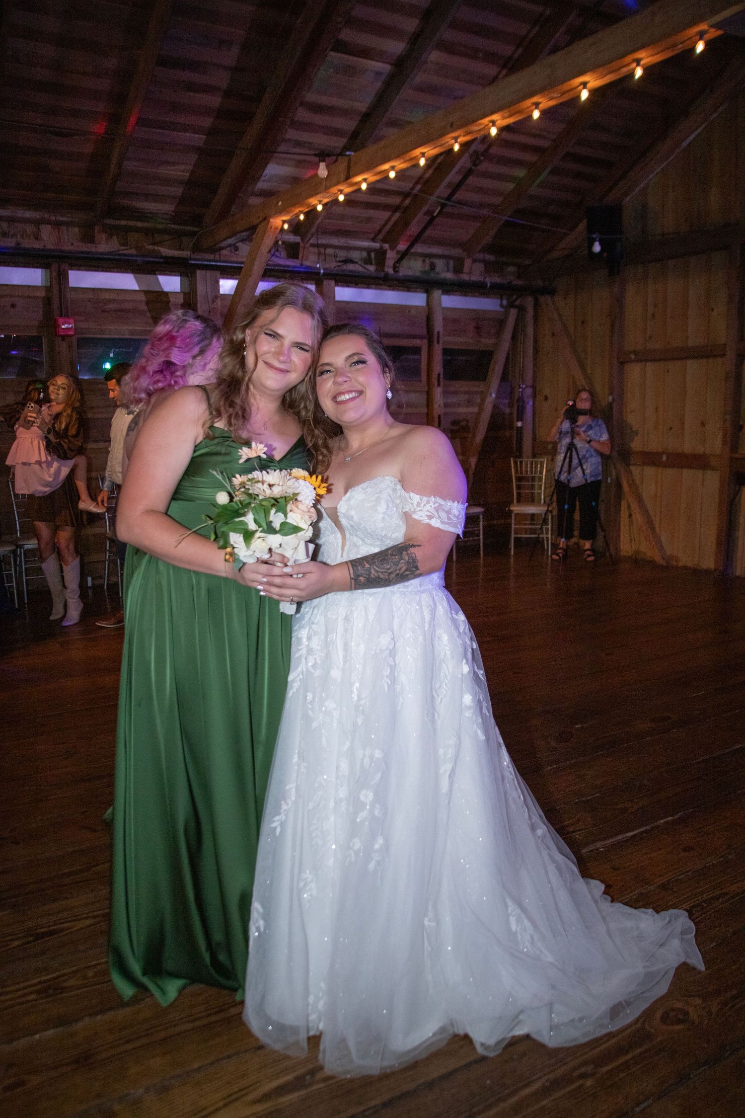 Two people in green and white formal dresses share a joyful moment during a rustic barn wedding reception.