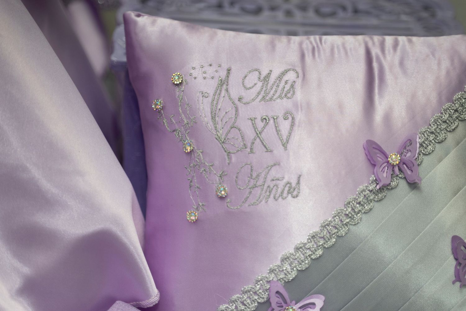 Close-up detail of lavender colored fabric with delicate lace trim and embroidered floral designs.