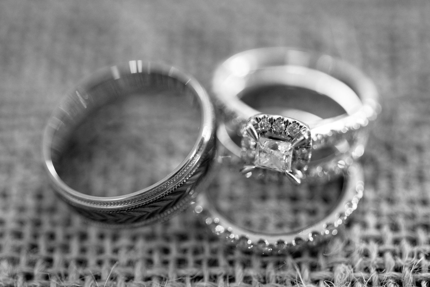 Close-up black and white photograph of diamond engagement rings on textured fabric.