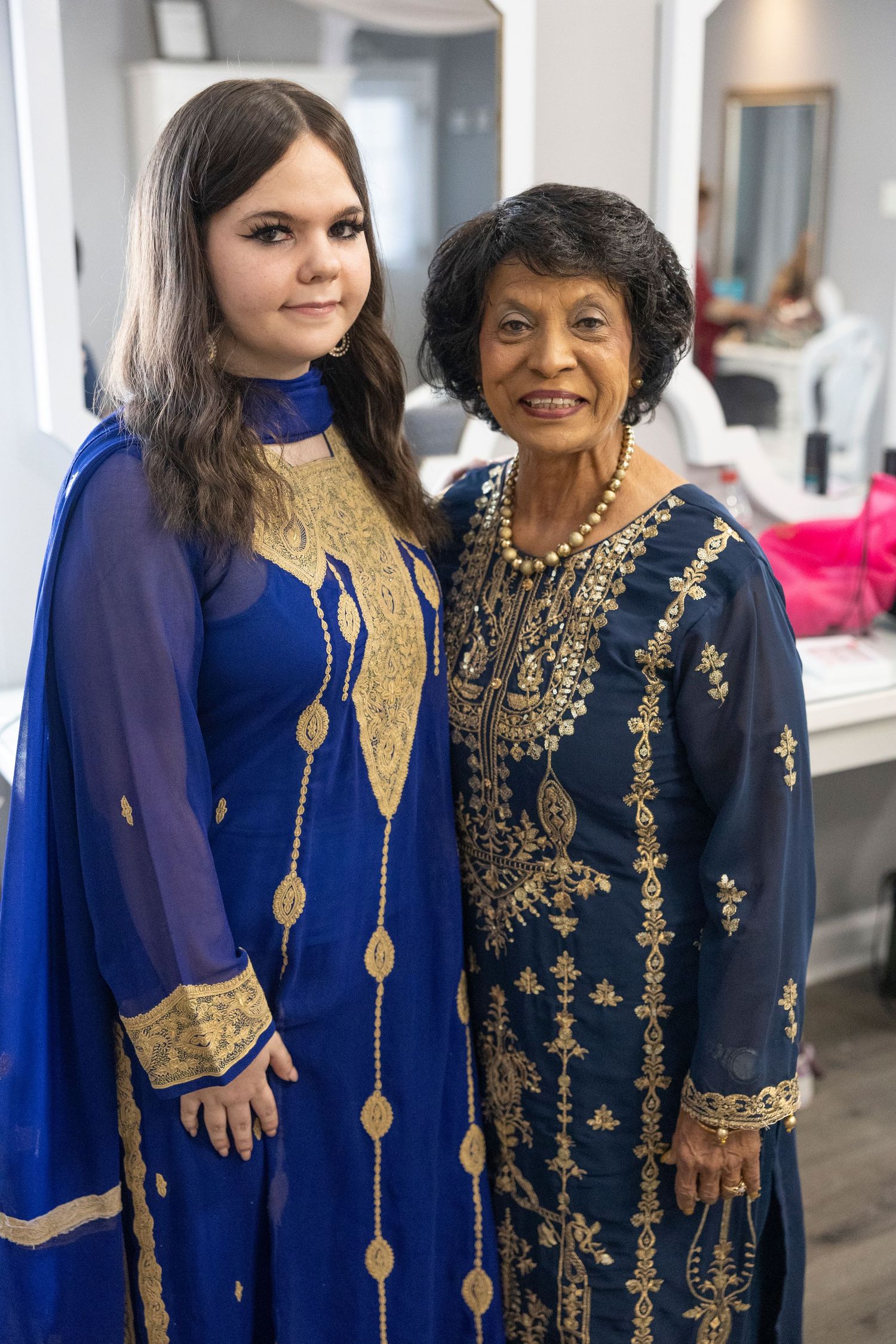 Two people wearing traditional Indian formal attire in navy blue and gold embroidery pose together for photos.