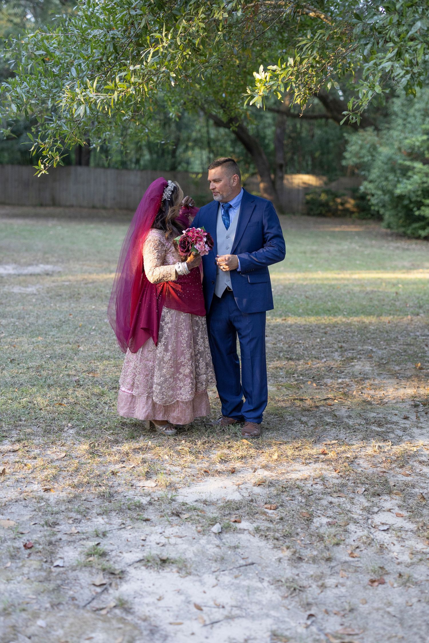 A couple in traditional wedding attire shares a romantic moment on fallen autumn leaves in a park setting.