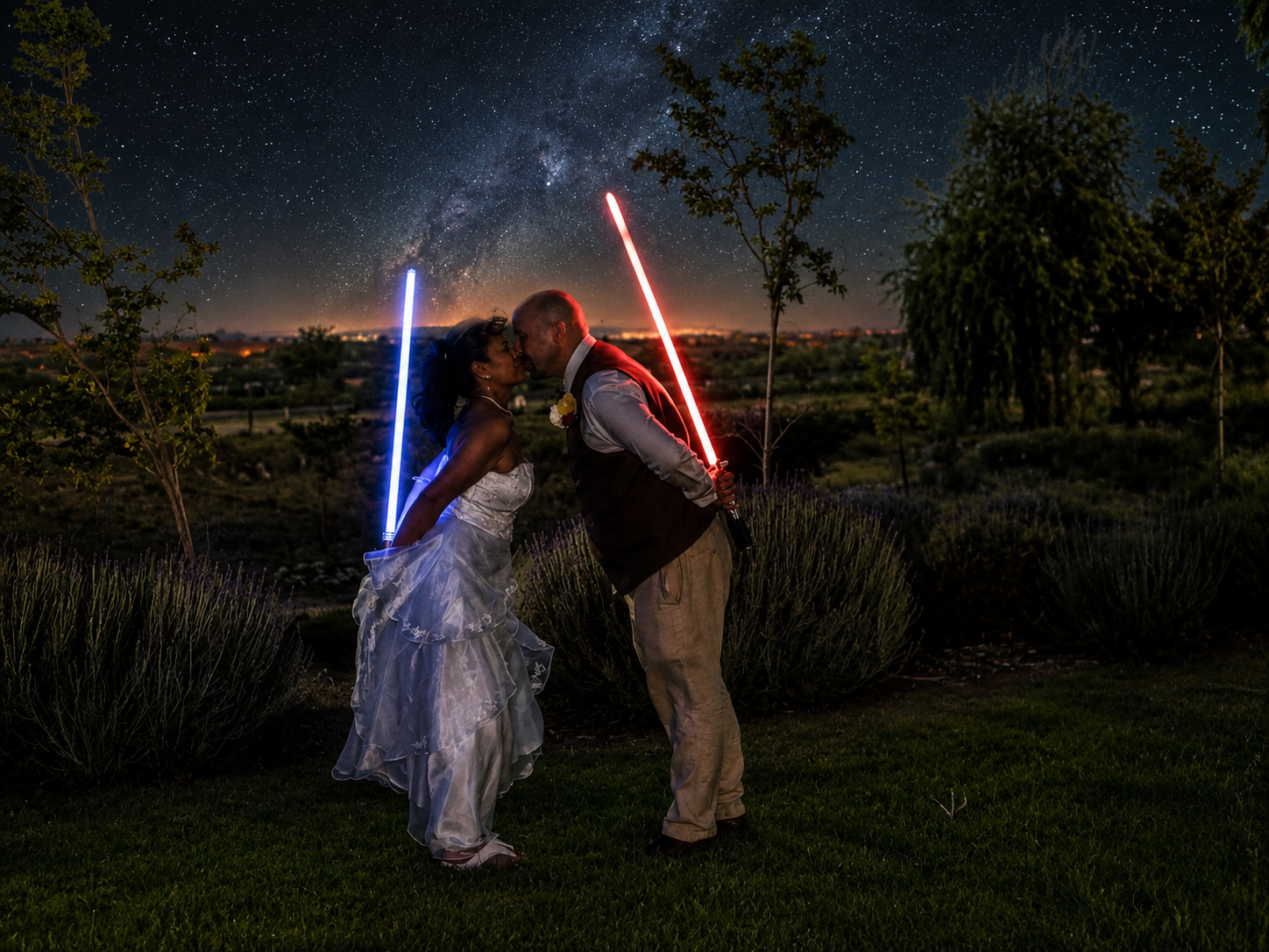 Bride and groom pose with glowing lightsabers under a stunning Milky Way night sky at their Star Wars wedding.