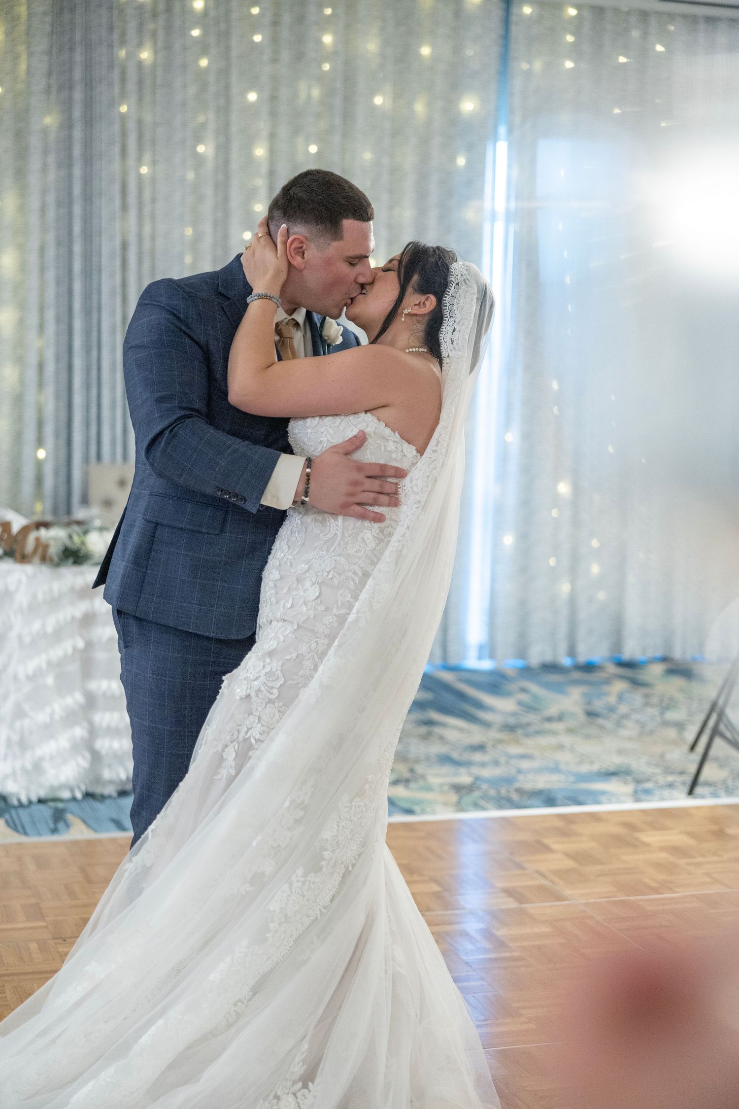 Bride and groom share a romantic first dance kiss in a ballroom adorned with twinkling fairy lights at their wedding reception.
