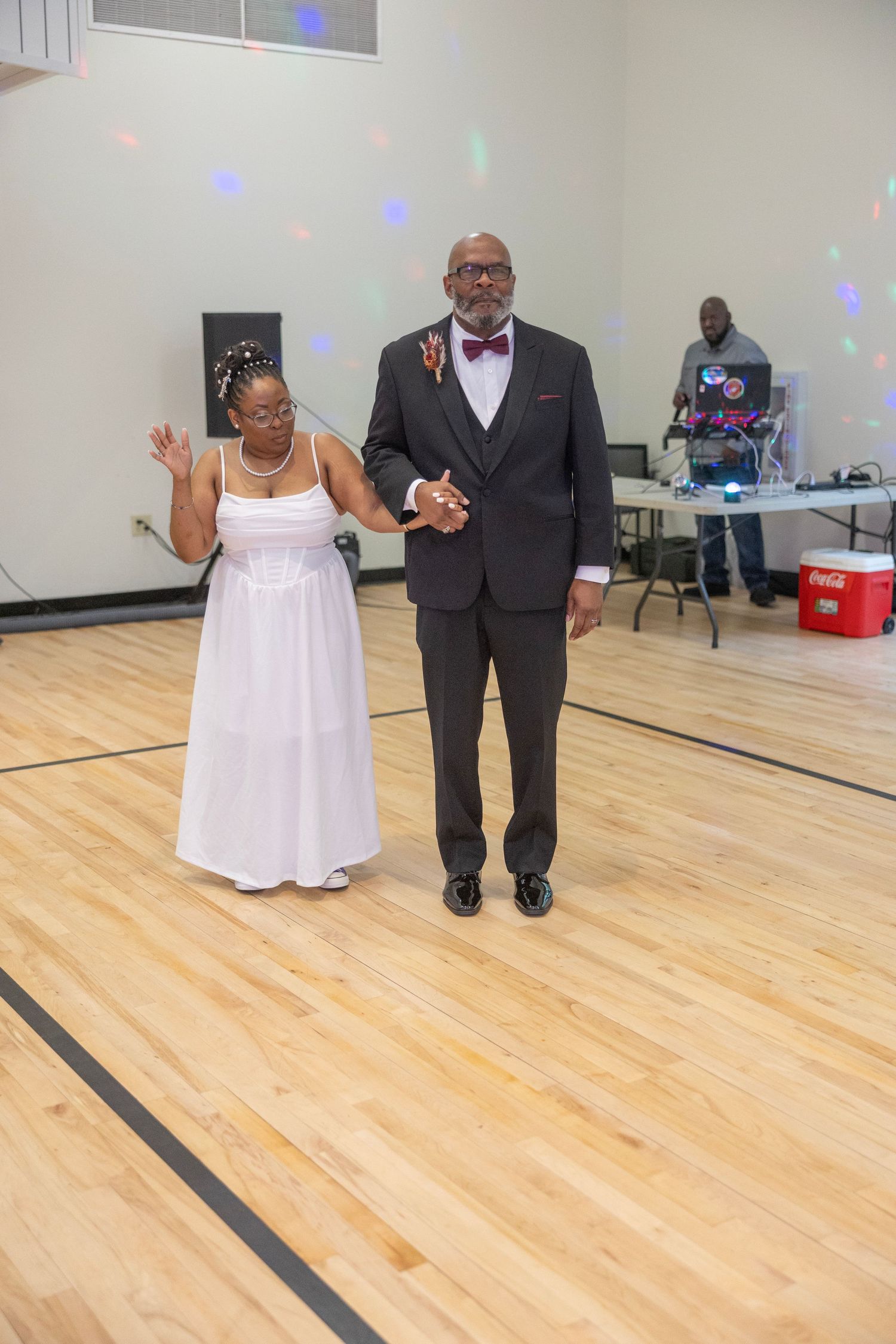 A couple in formal attire dancing together on a polished wooden floor in what appears to be a community center.
