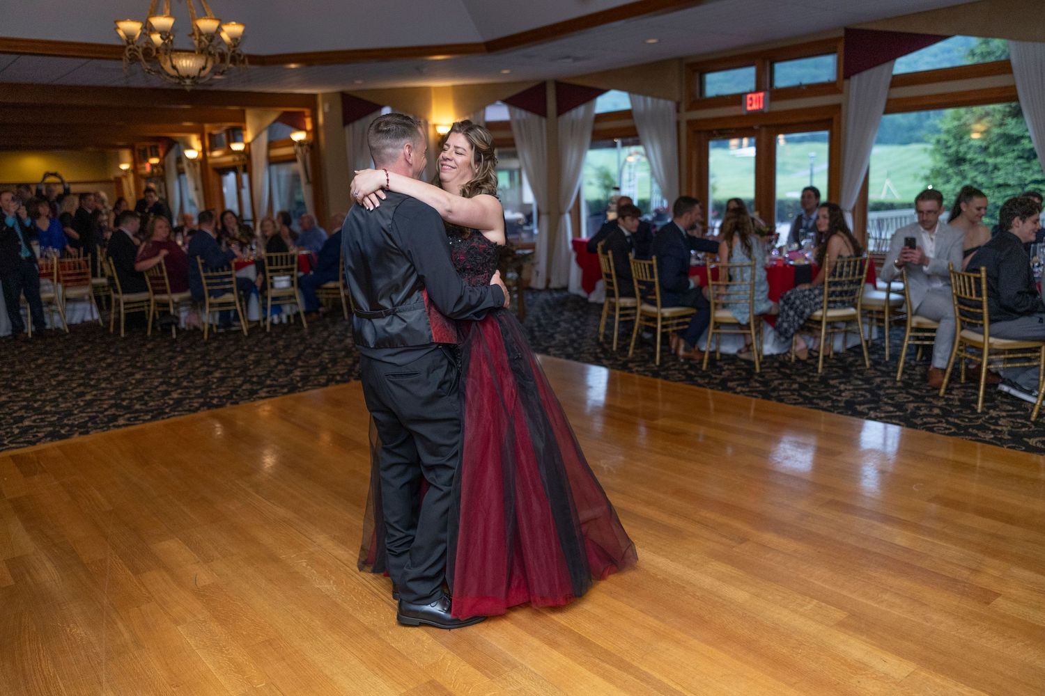 Couples dance together on a polished wooden floor in a spacious ballroom with warm lighting.