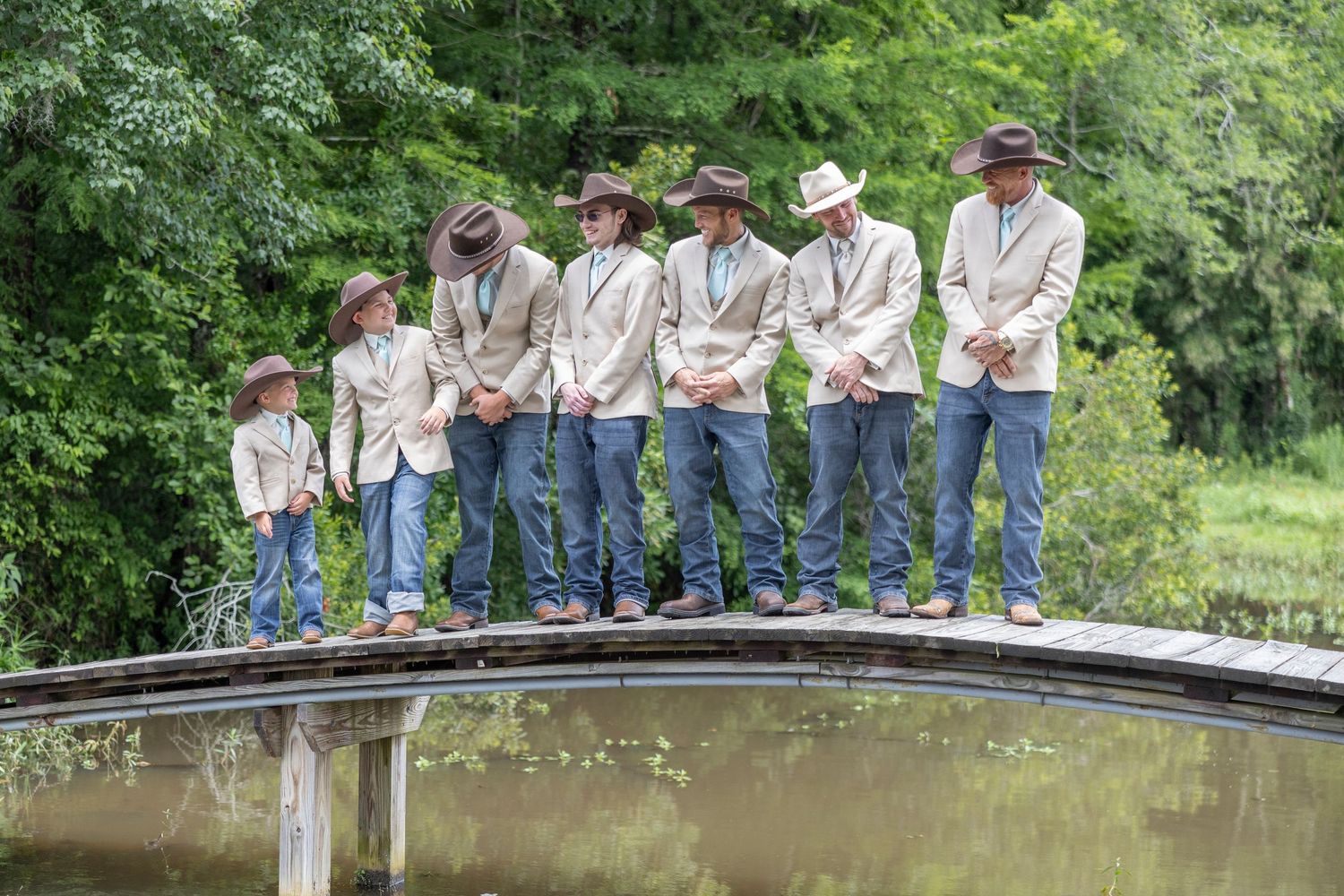 A group of people in matching light colored shirts and cowboy hats stand in line on a curved wooden bridge.