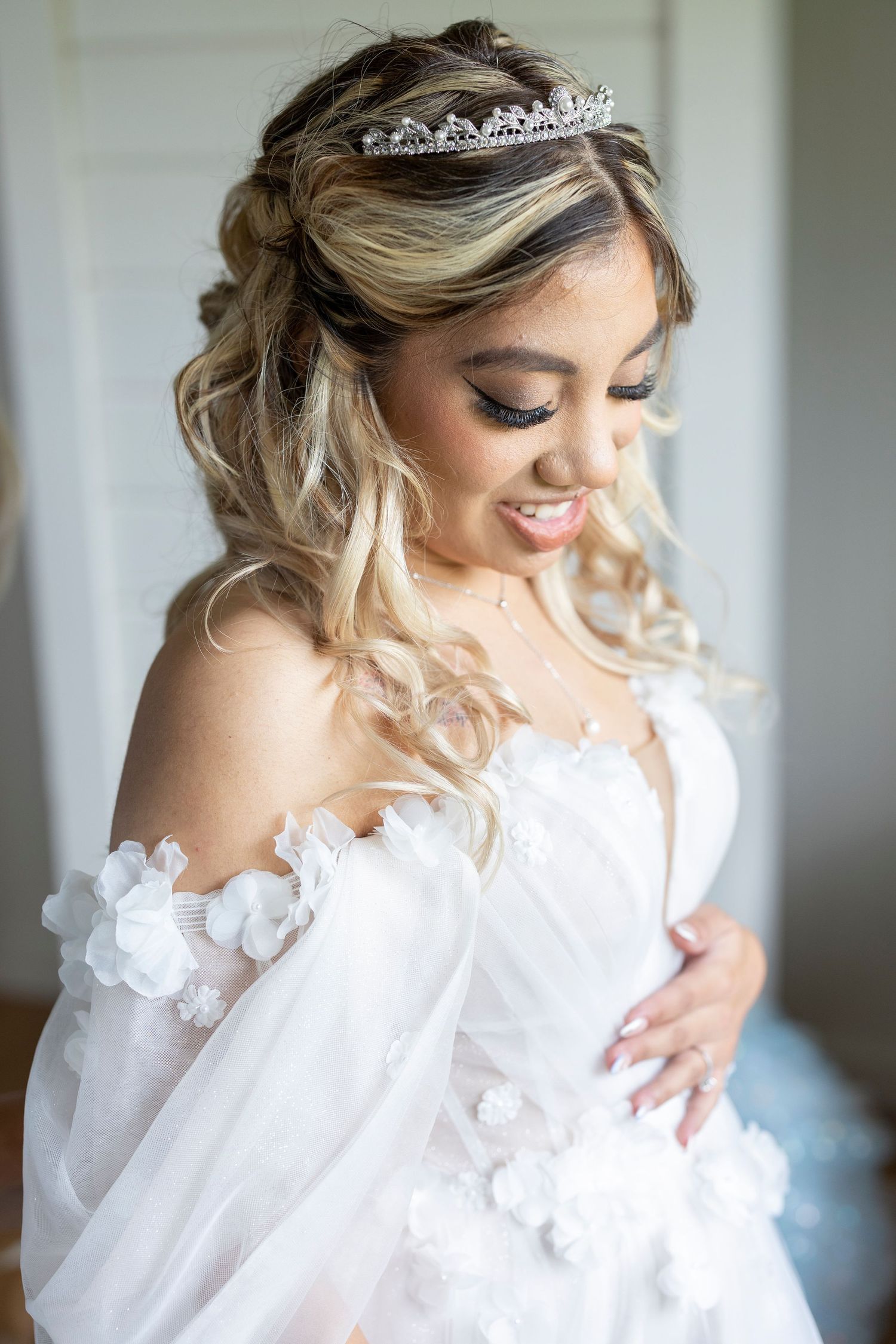 A bride in a white gown with butterfly details and tiara smiles while looking down in a series of wedding portraits.