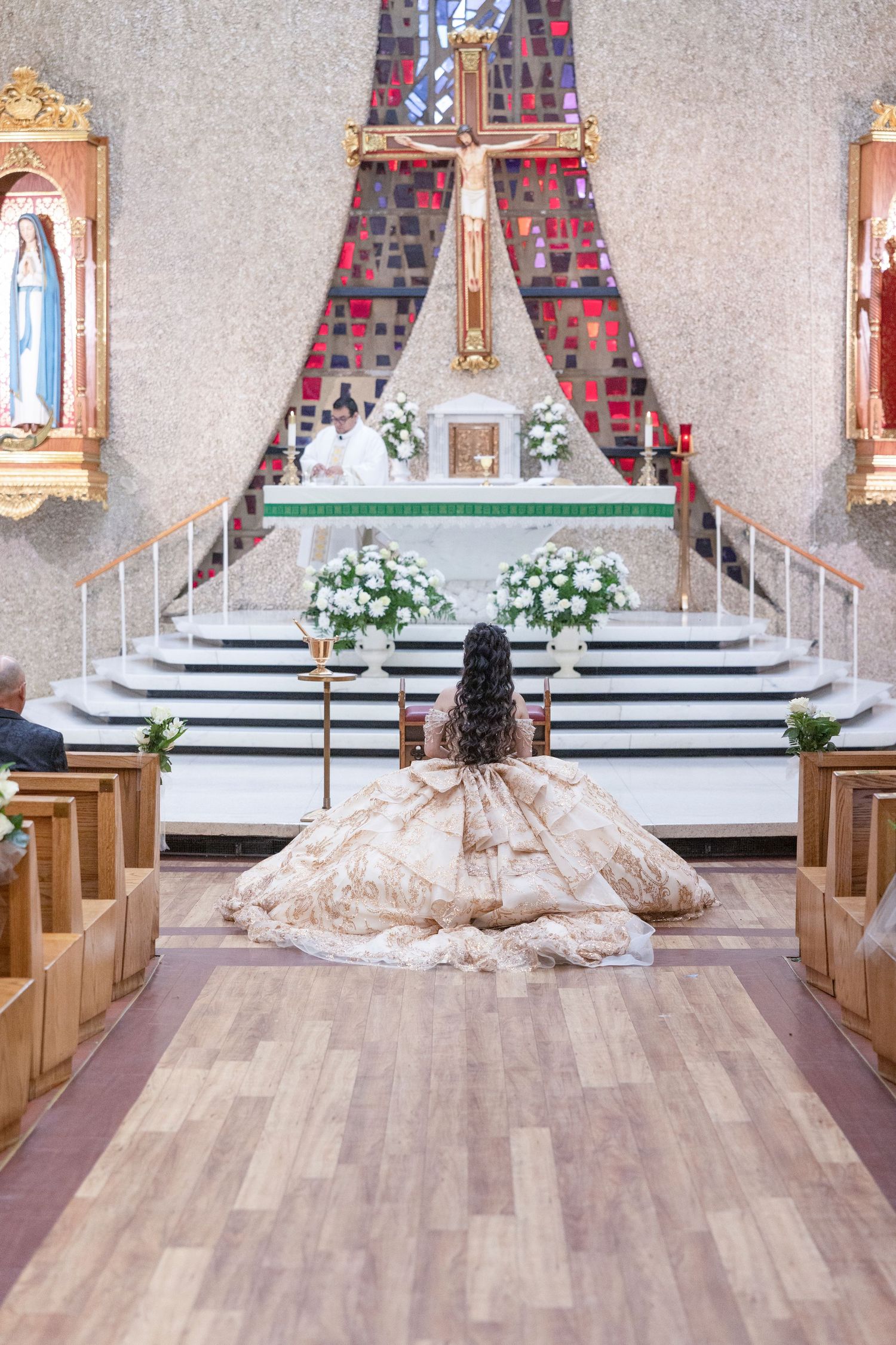 Young woman in a ballgown kneels before a church altar during a Quinceañera ceremony.
