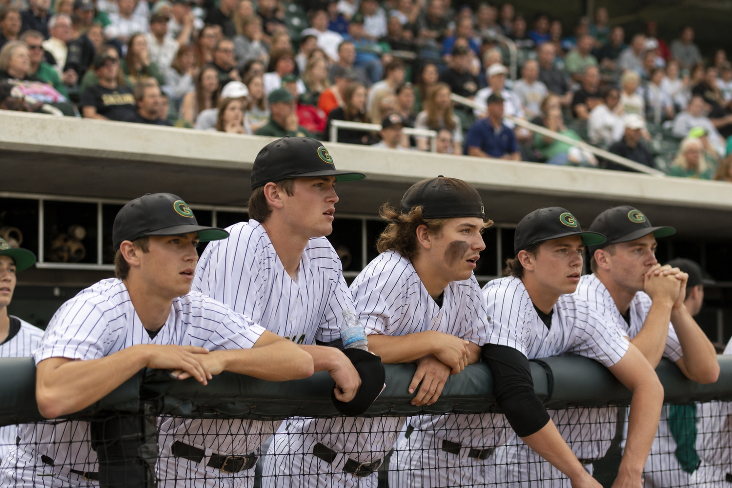 Five baseball players in pinstripe uniforms lean on dugout railing watching the game intently.