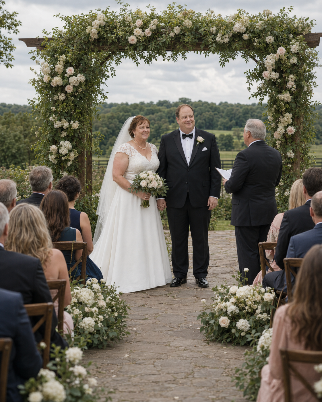Bride and groom stand under floral arch at outdoor wedding ceremony with guests seated along aisle.
