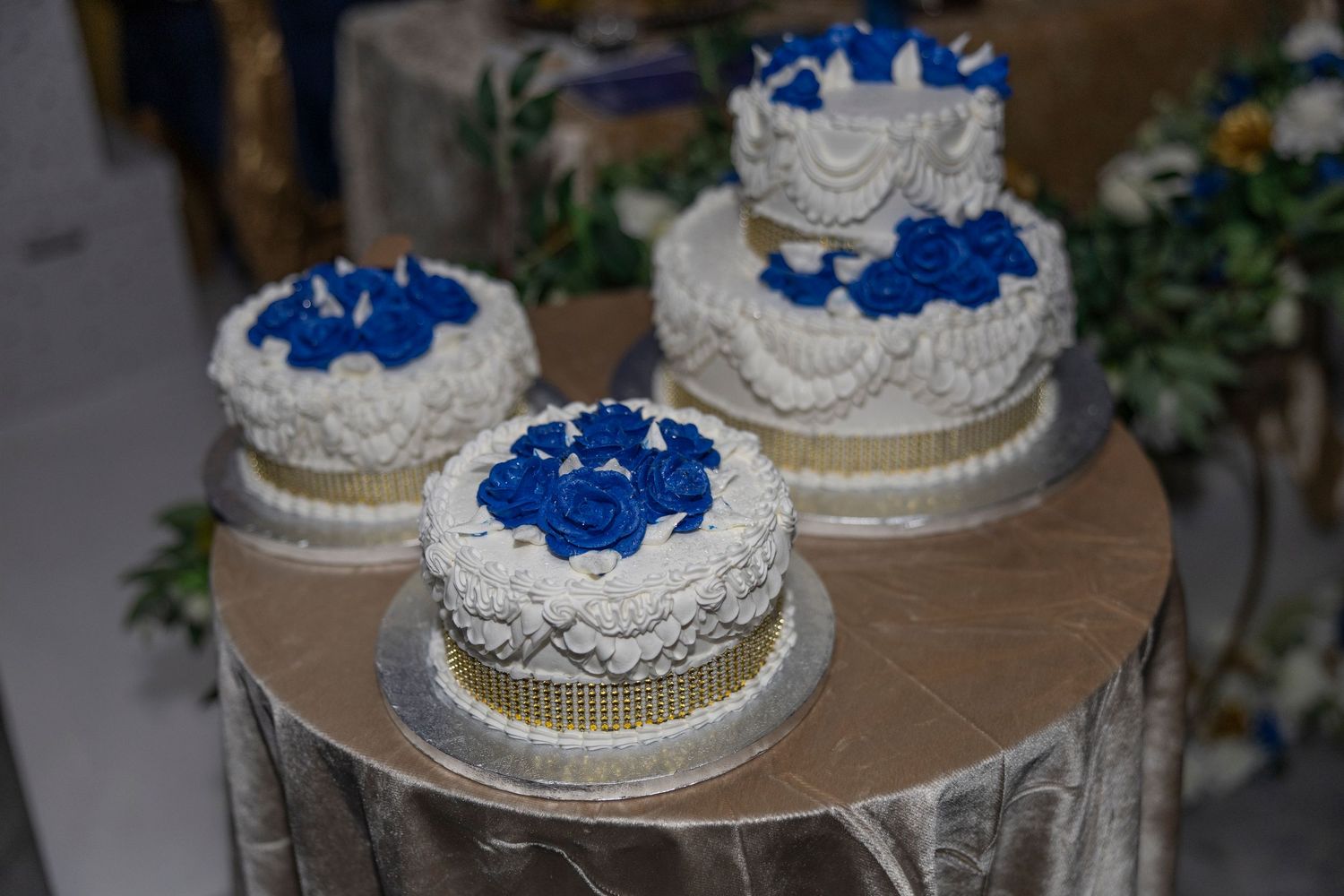 White wedding cakes decorated with blue frosting roses displayed on silver stands at a reception.