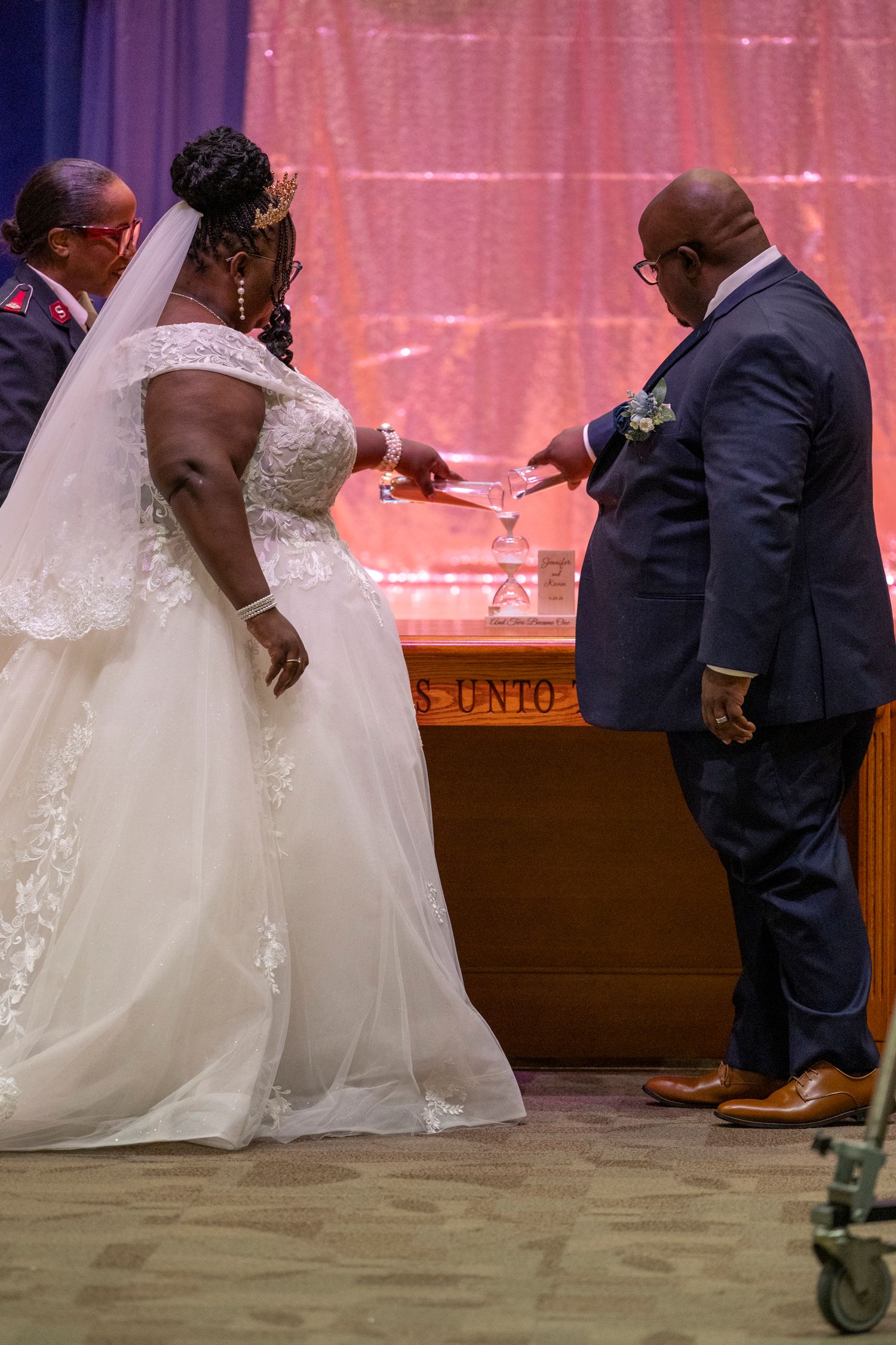 Bride and groom exchanging rings during wedding ceremony, bride in lace gown with veil, groom in navy suit.