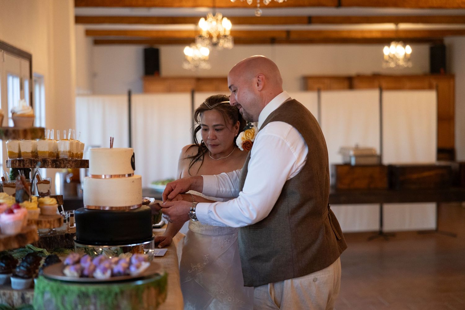 Bride and groom cutting their wedding cake together at a rustic indoor reception venue.