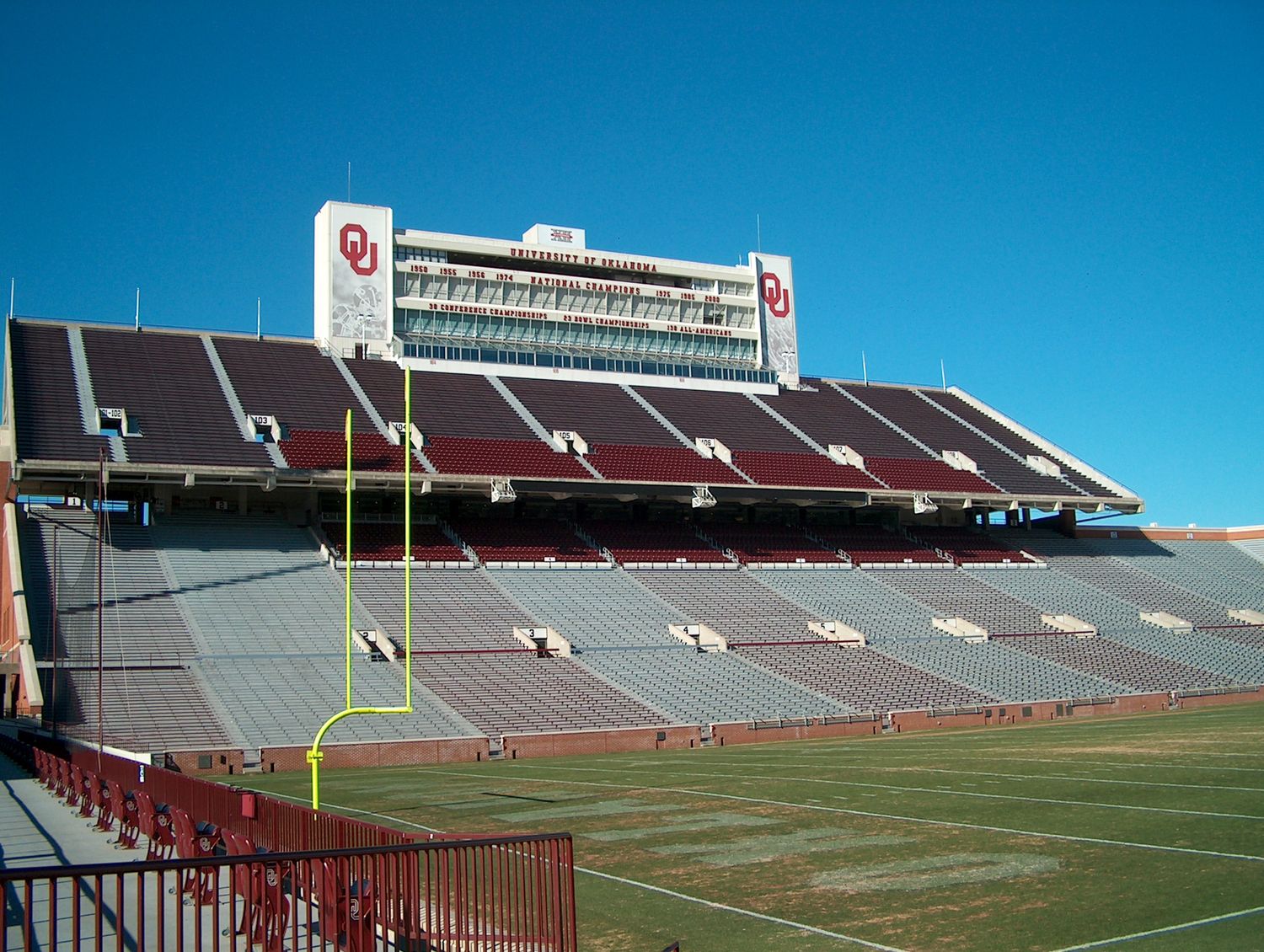 Memorial Stadium at the University of Oklahoma features red stadium seating and goalposts under bright blue skies.