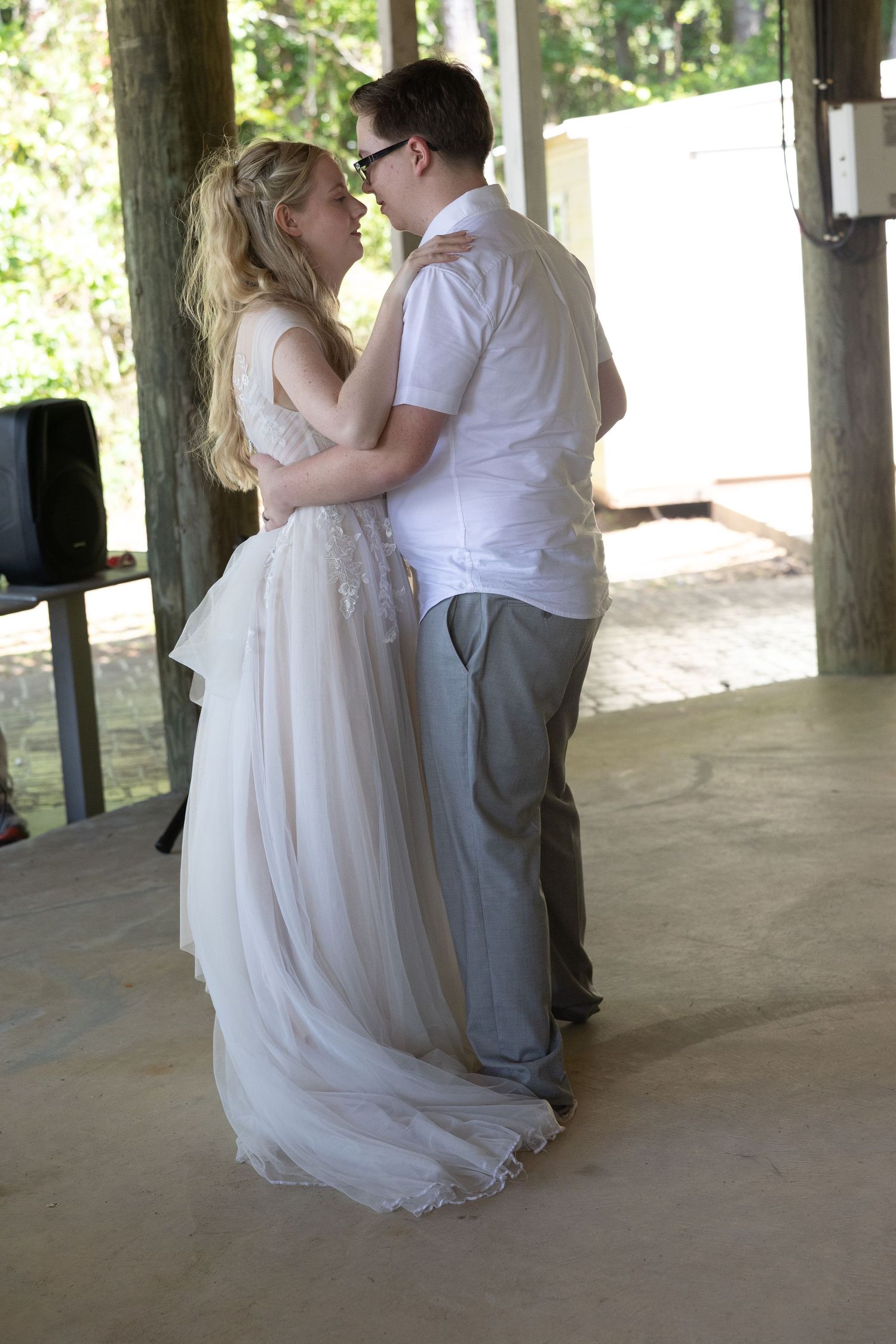 A couple shares their first dance under a rustic covered outdoor venue during a wedding celebration.