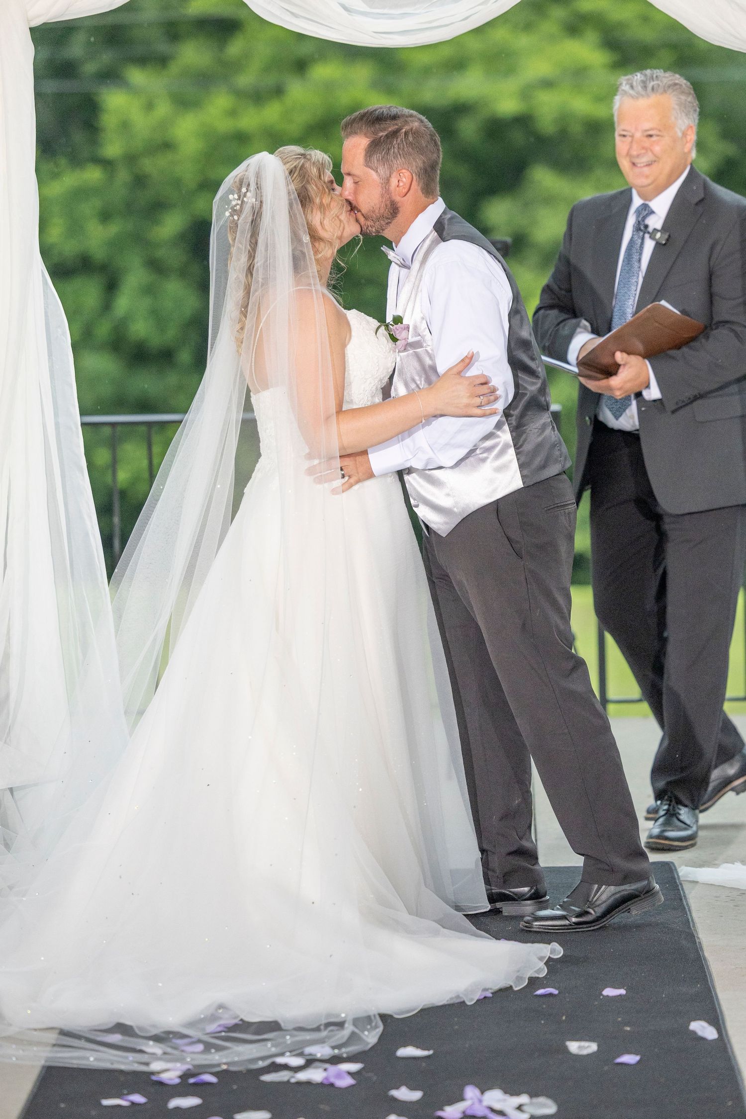 A wedding couple shares their first dance under a white gazebo with flower petals scattered on the ground.