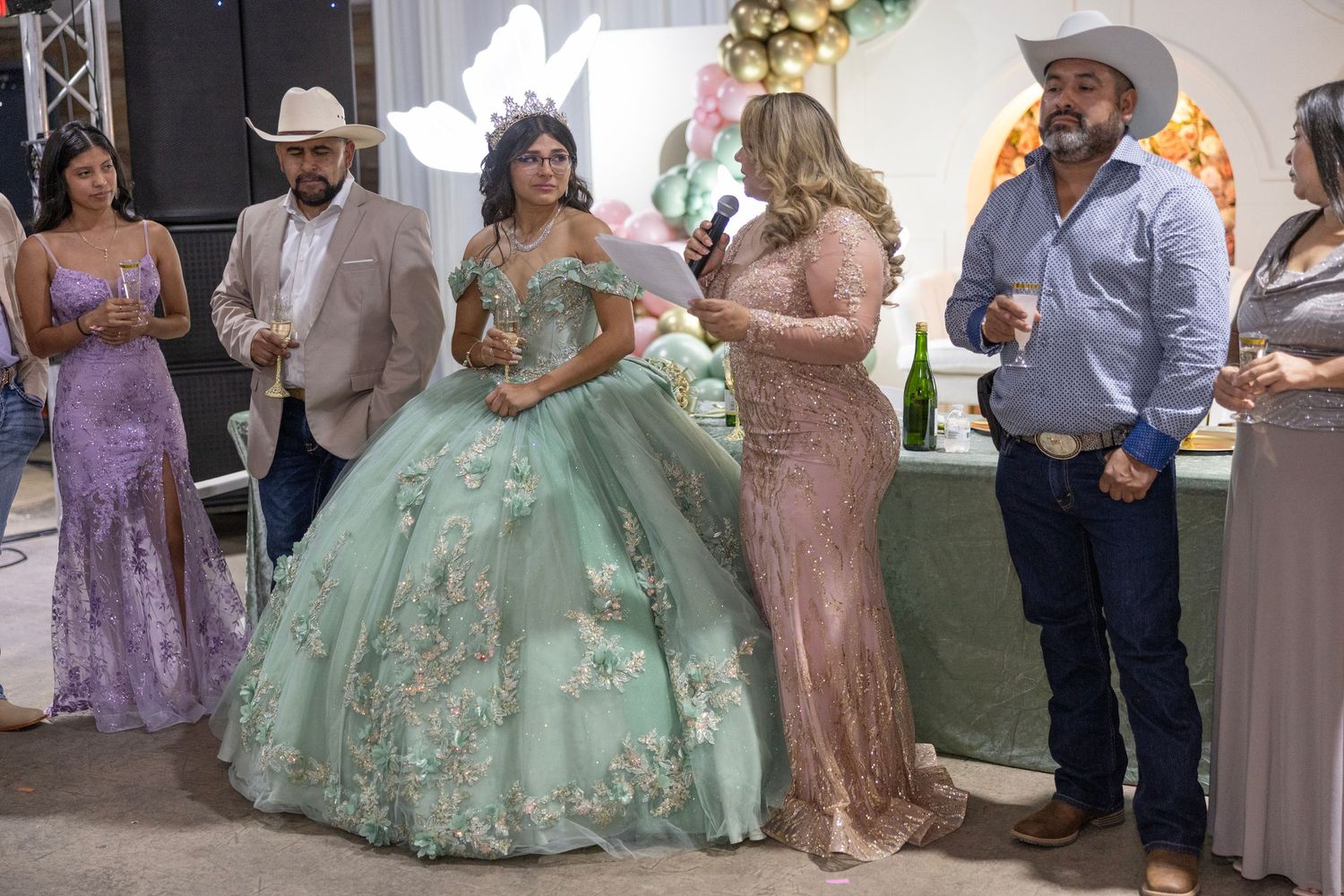 A group of people in formal attire gather at a celebration event with decorative floral arrangements.