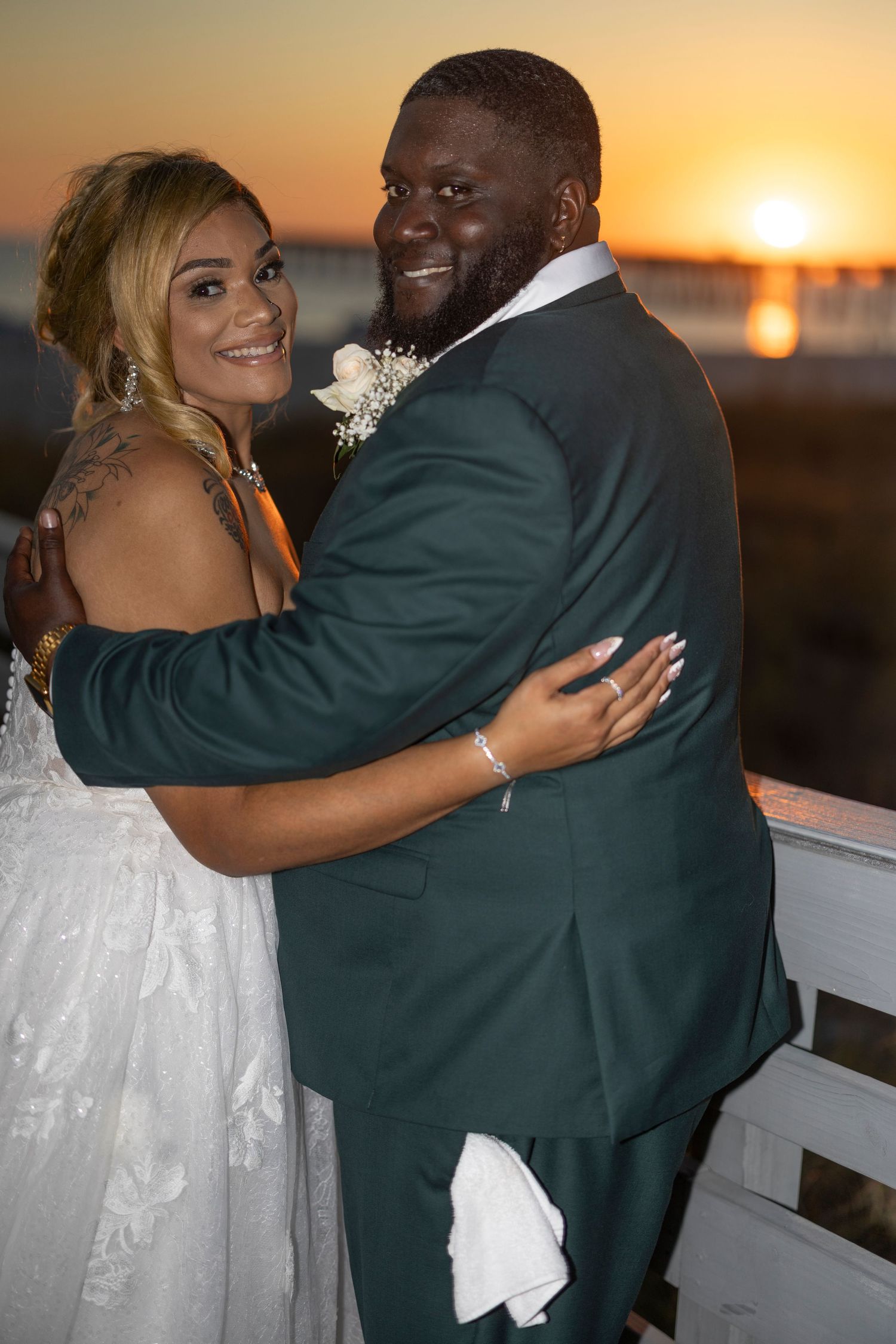 A couple embraces during sunset at their outdoor wedding celebration, creating a romantic silhouette against the golden sky.