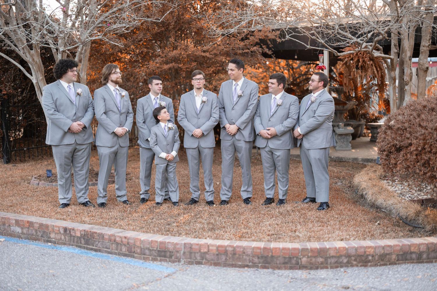 Wedding party in light gray suits standing outdoors on brick pathway during autumn.