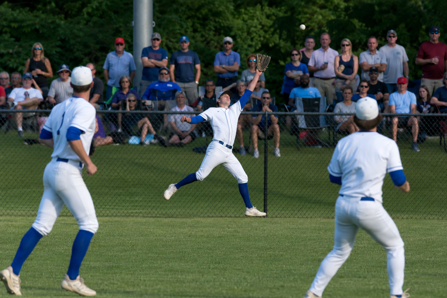 Baseball outfielders in white uniforms converge to catch a fly ball during a sunny game.