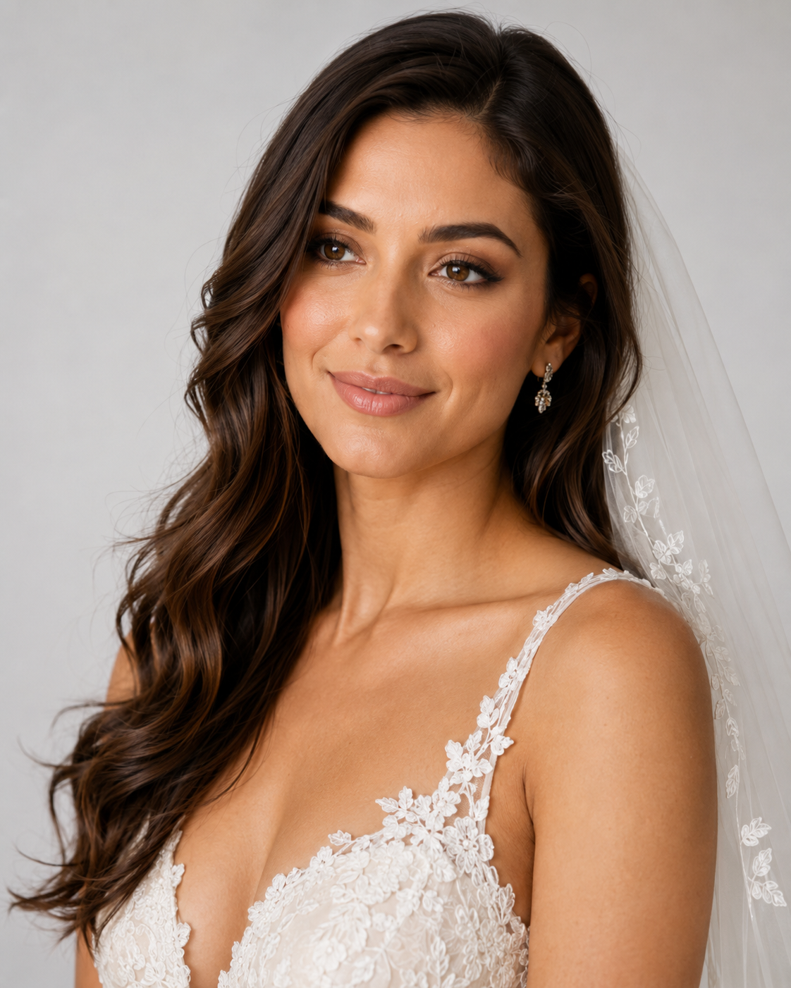 Bride wearing lace wedding dress and veil with gold drop earrings, long dark wavy hair, soft bridal makeup.