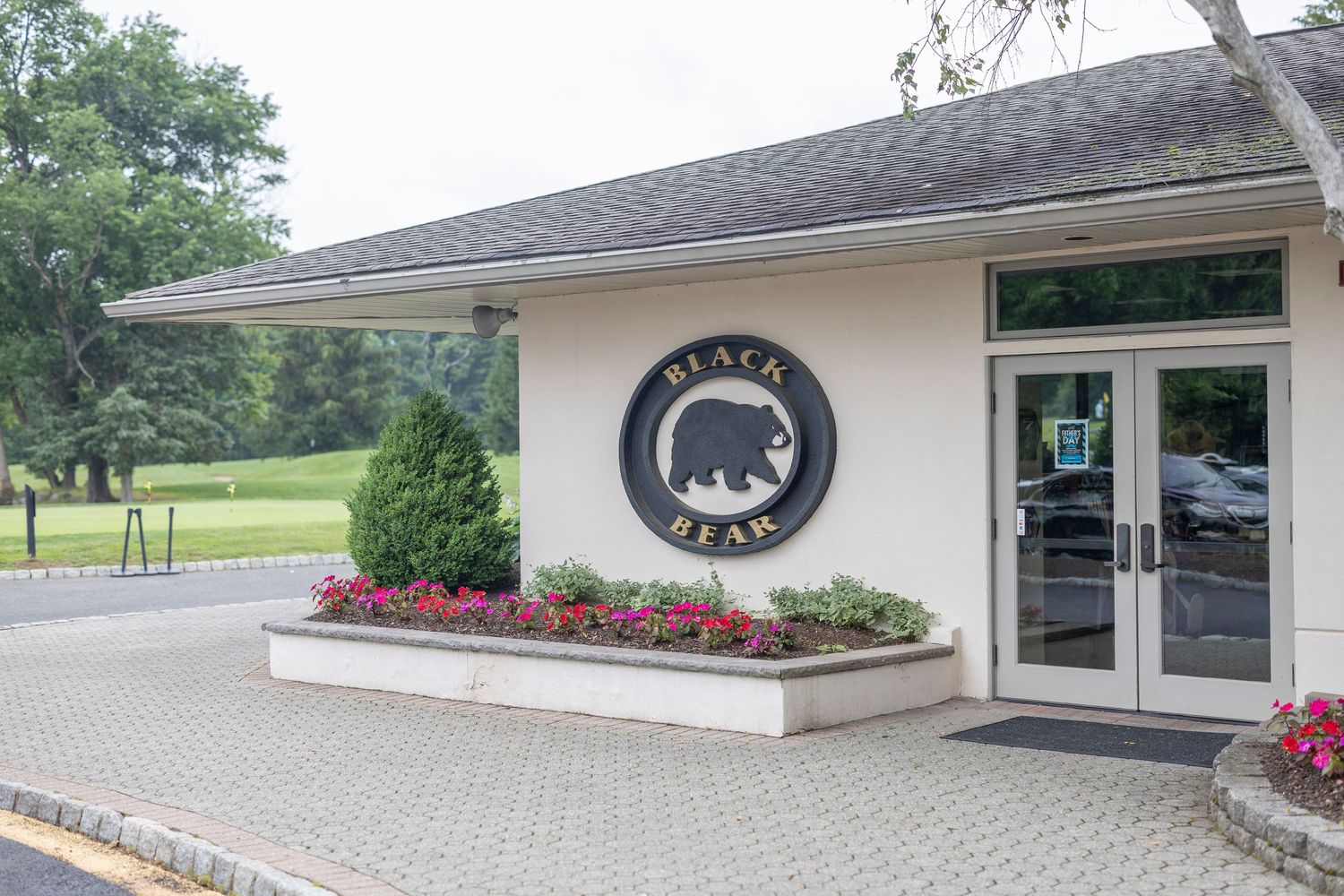 Small white building entrance with Black Bear logo and red flower landscaping at the entrance.