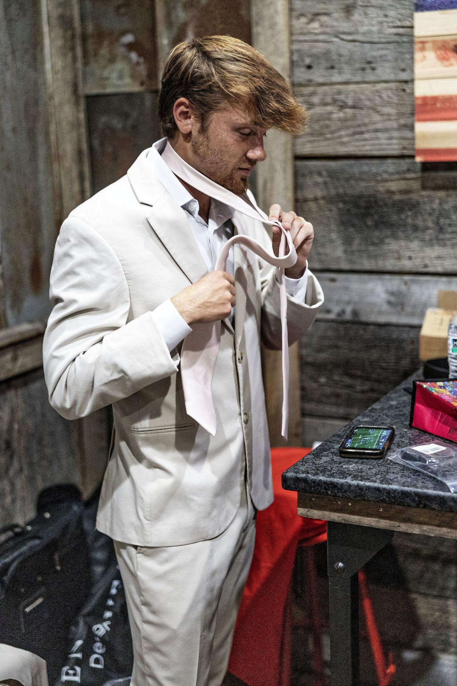 A sequence of images shows someone in a white suit adjusting their tie against a rustic wooden wall background.