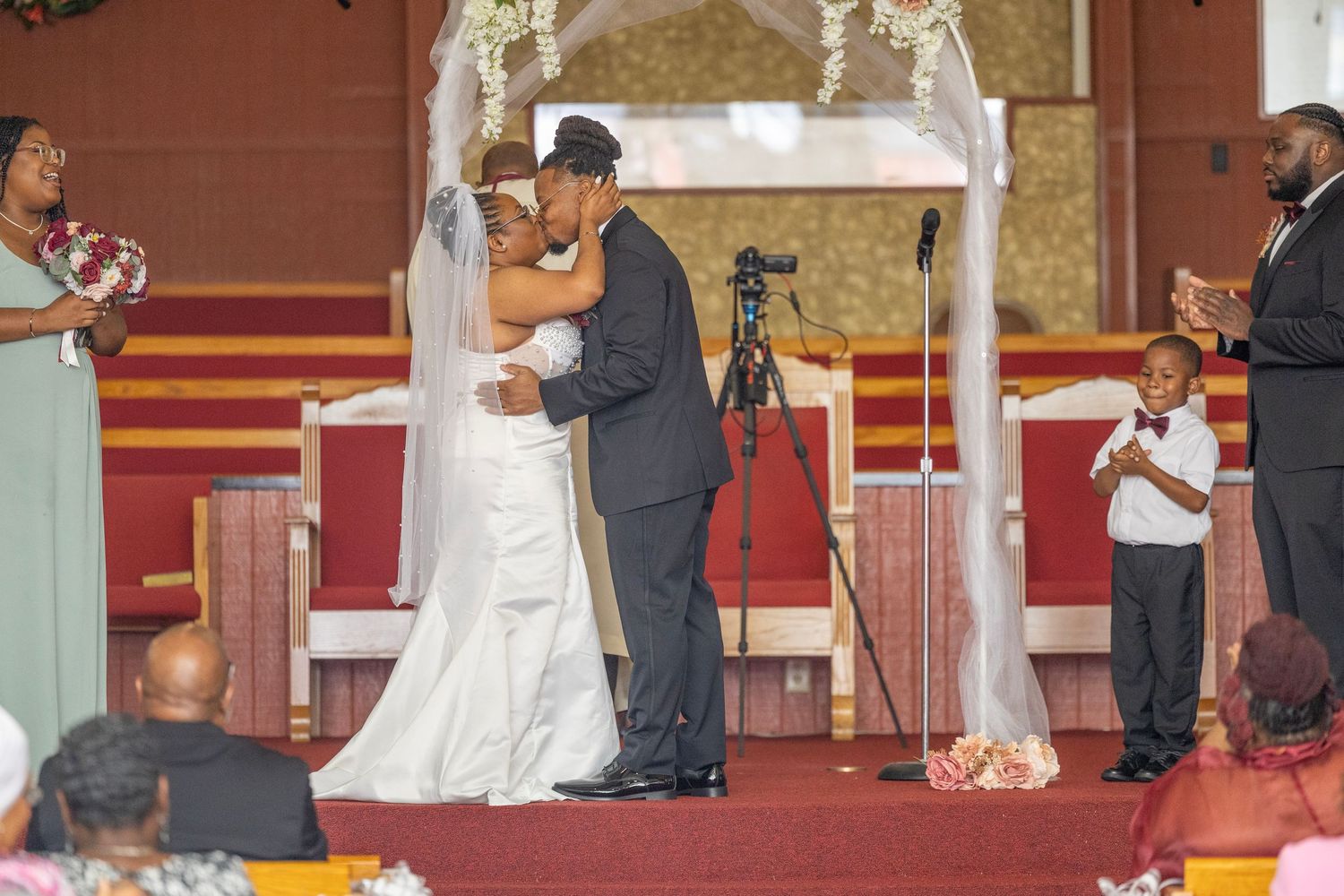 A couple shares their first kiss as newlyweds under a decorated arch at the altar during their wedding ceremony.