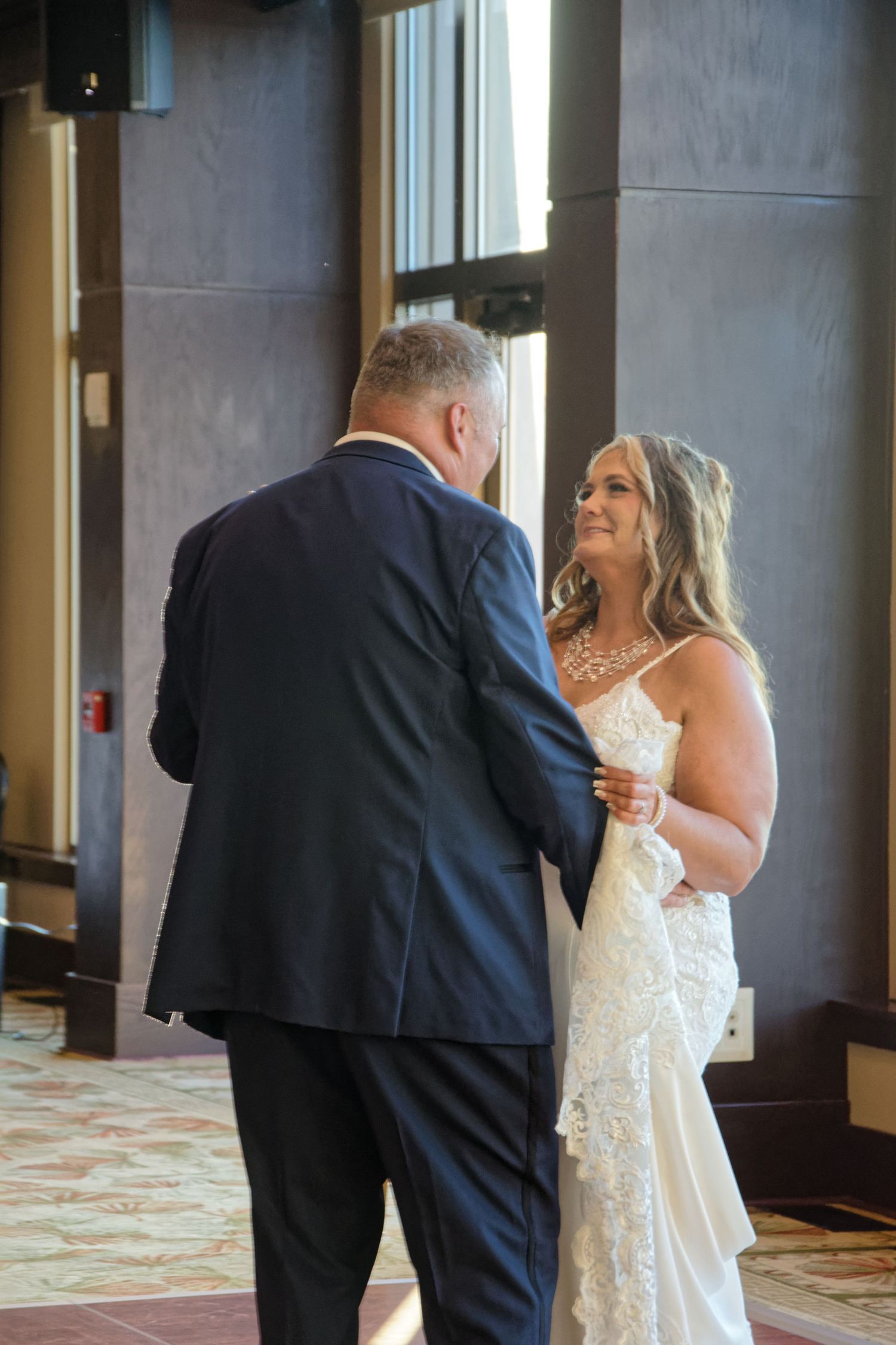 A bride and father share an emotional first look moment in an elegant hotel hallway.