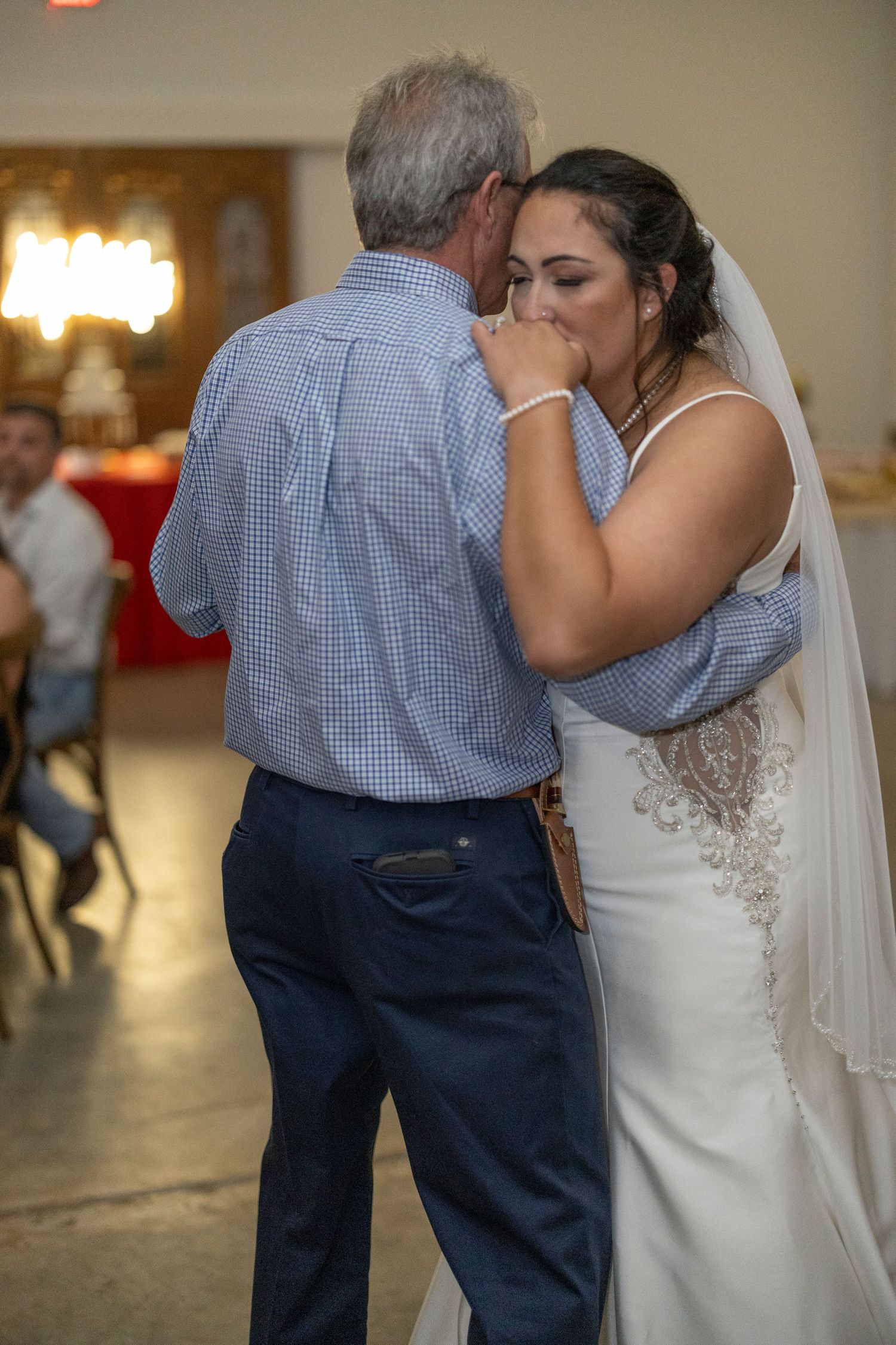 An emotional moment during a wedding dance as a bride in a white gown shares a dance with someone in a blue checkered shirt.