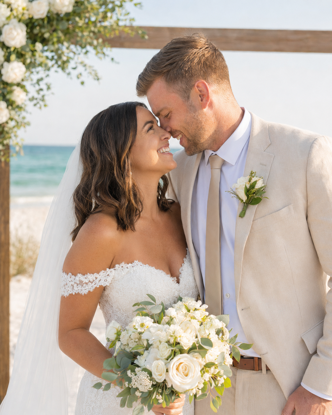 Bride and groom share a romantic moment at a beach wedding, with white floral bouquet and arch backdrop.