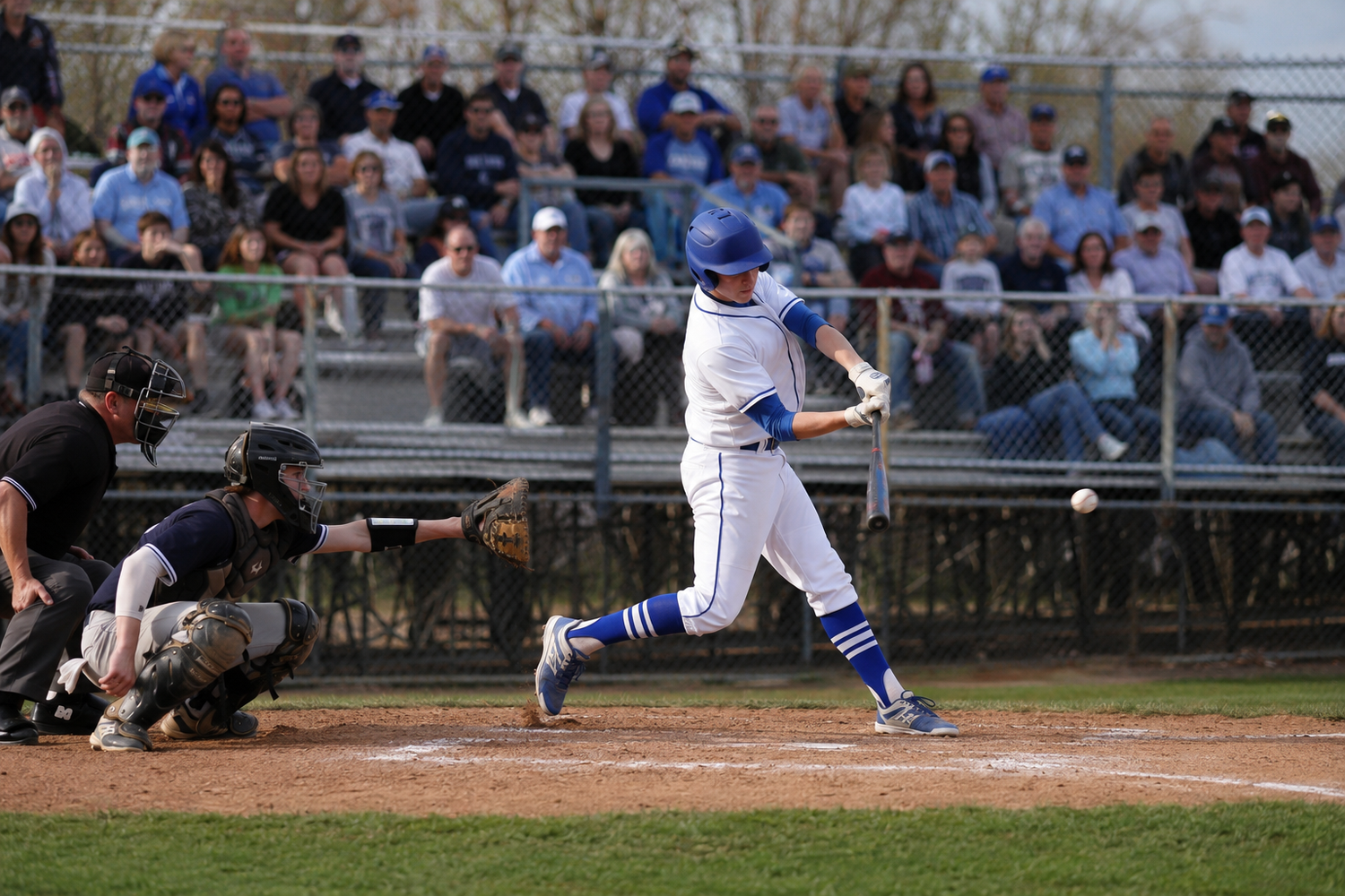 Baseball player in blue and white uniform swings bat during a game with fans in background.