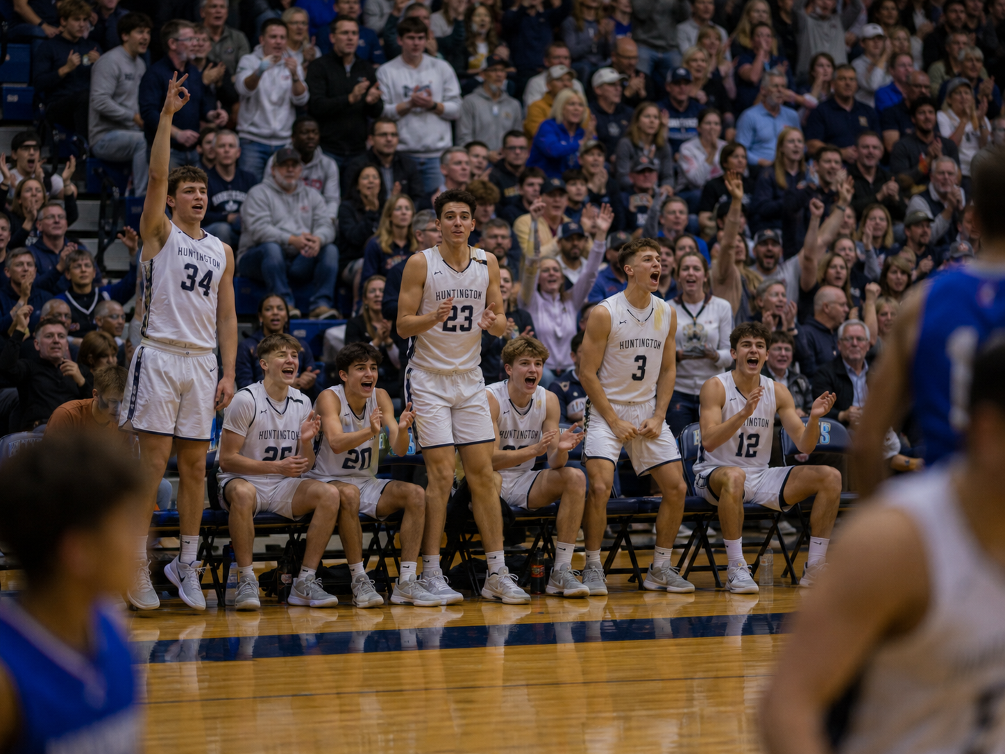 High school basketball players celebrate on the bench during an exciting game in a packed gymnasium.