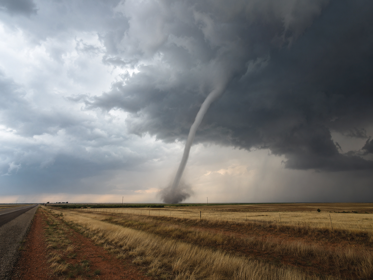 A massive tornado touches down on flat prairie land under dramatic storm clouds in the Great Plains.