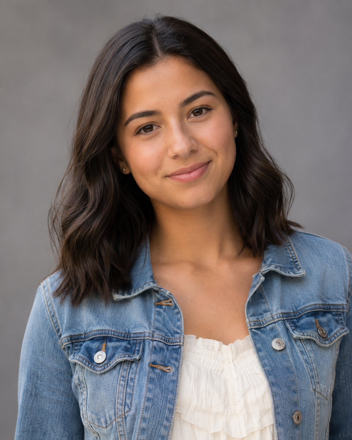 Young brunette woman in denim jacket and white top smiling in professional headshot.