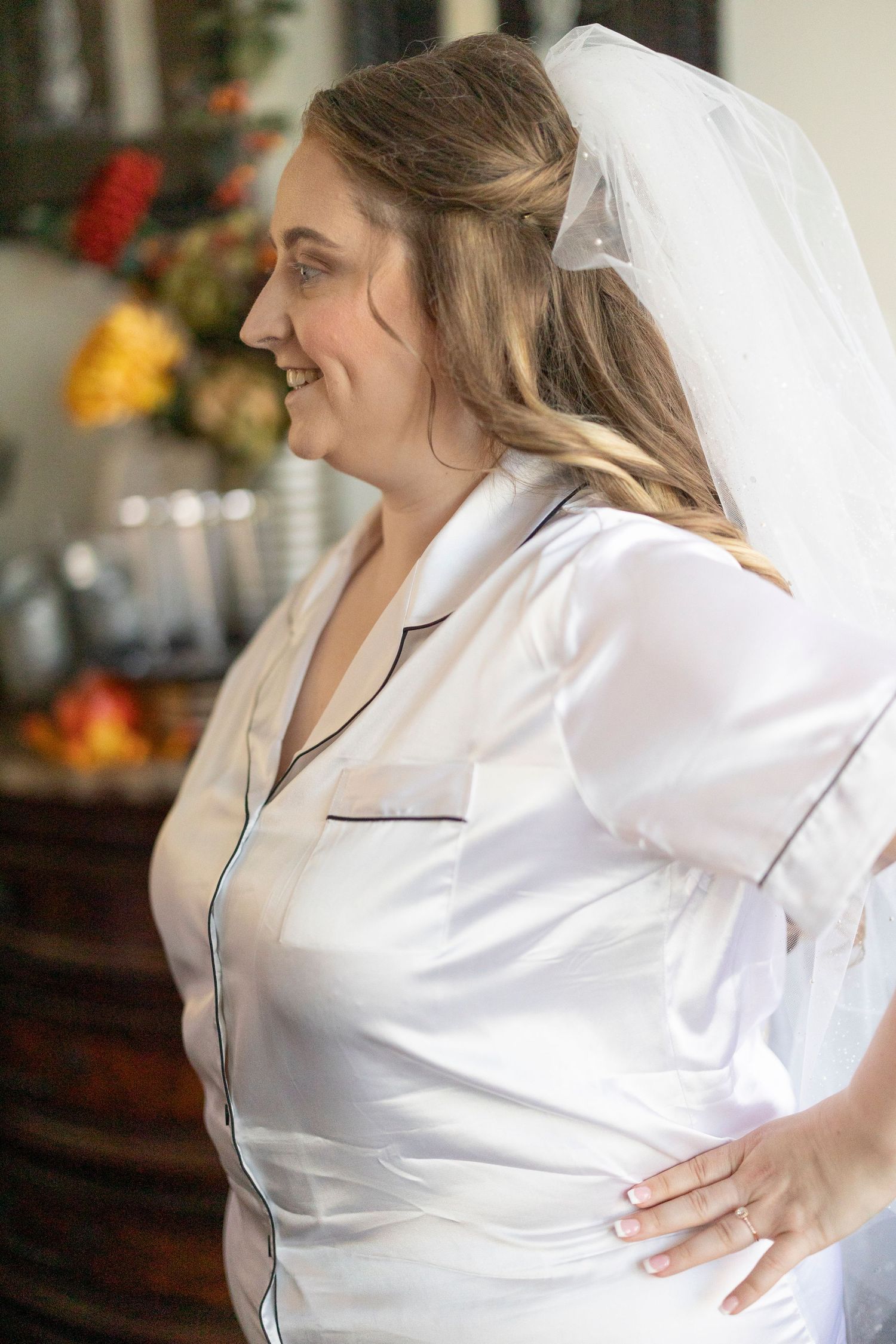 A bride in a white silk robe smiles while getting ready on her wedding morning.