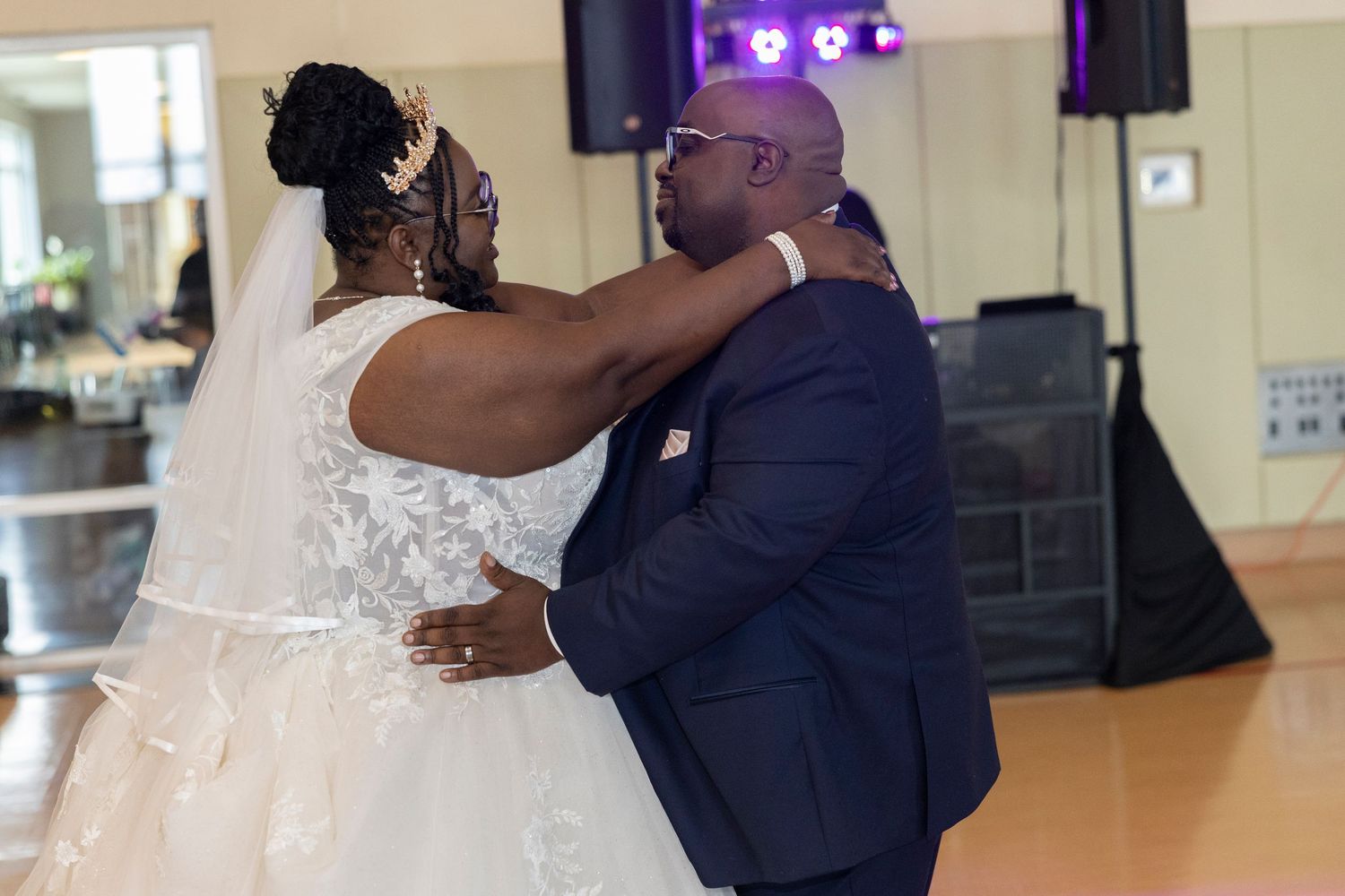 Bride and groom share their first dance at wedding reception, wearing white gown and navy suit.