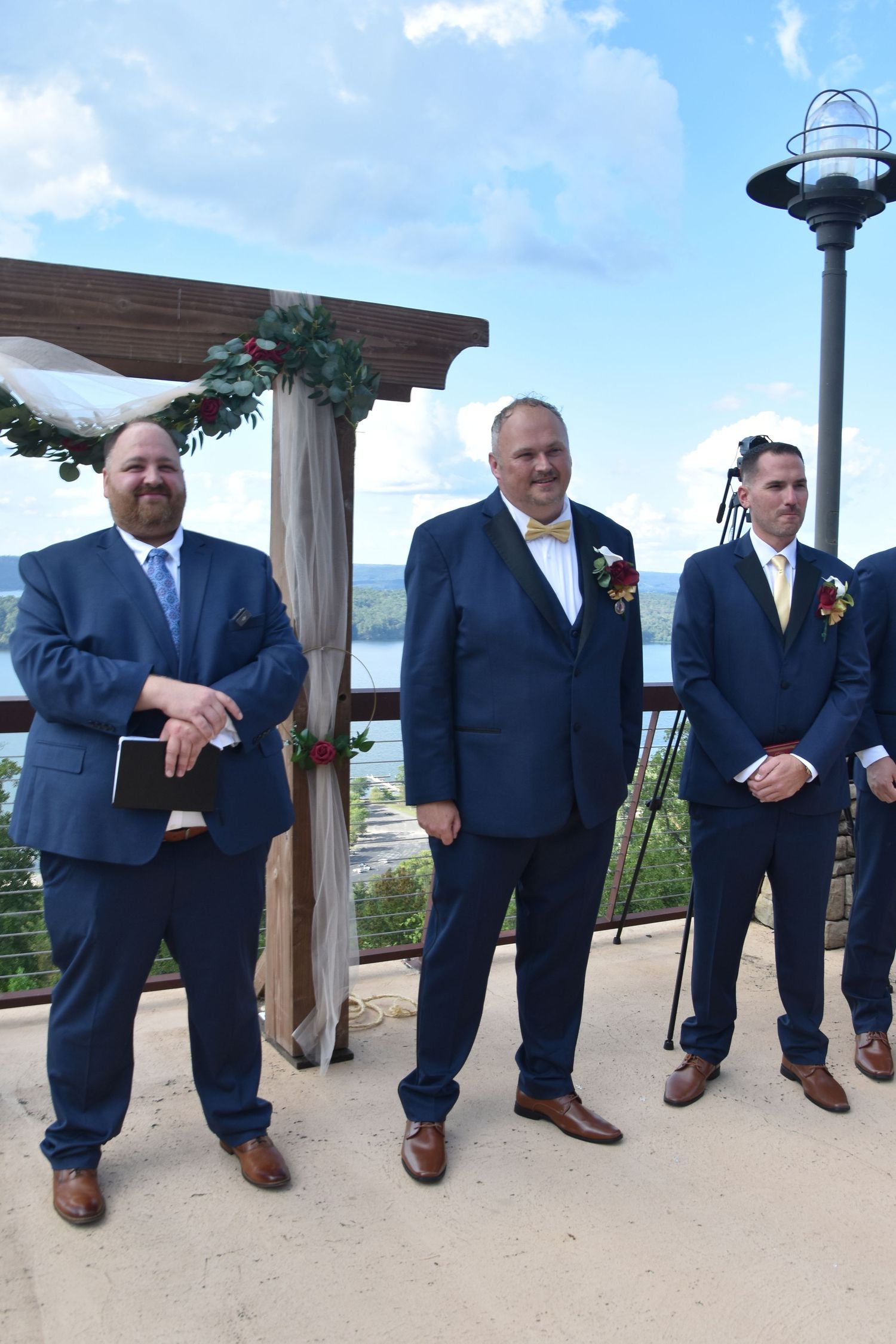 A group of groomsmen in navy suits sit lined up on a ledge showing off their brown dress shoes and socks.