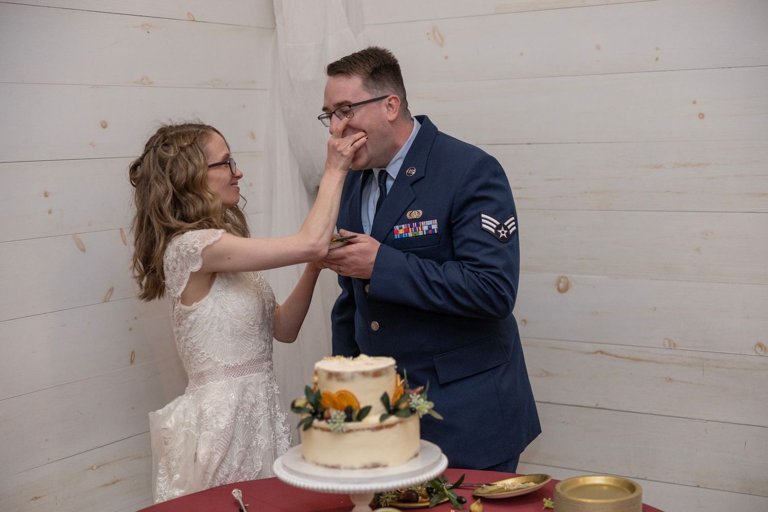 Couple playfully smashes wedding cake into each other's faces during reception celebration.